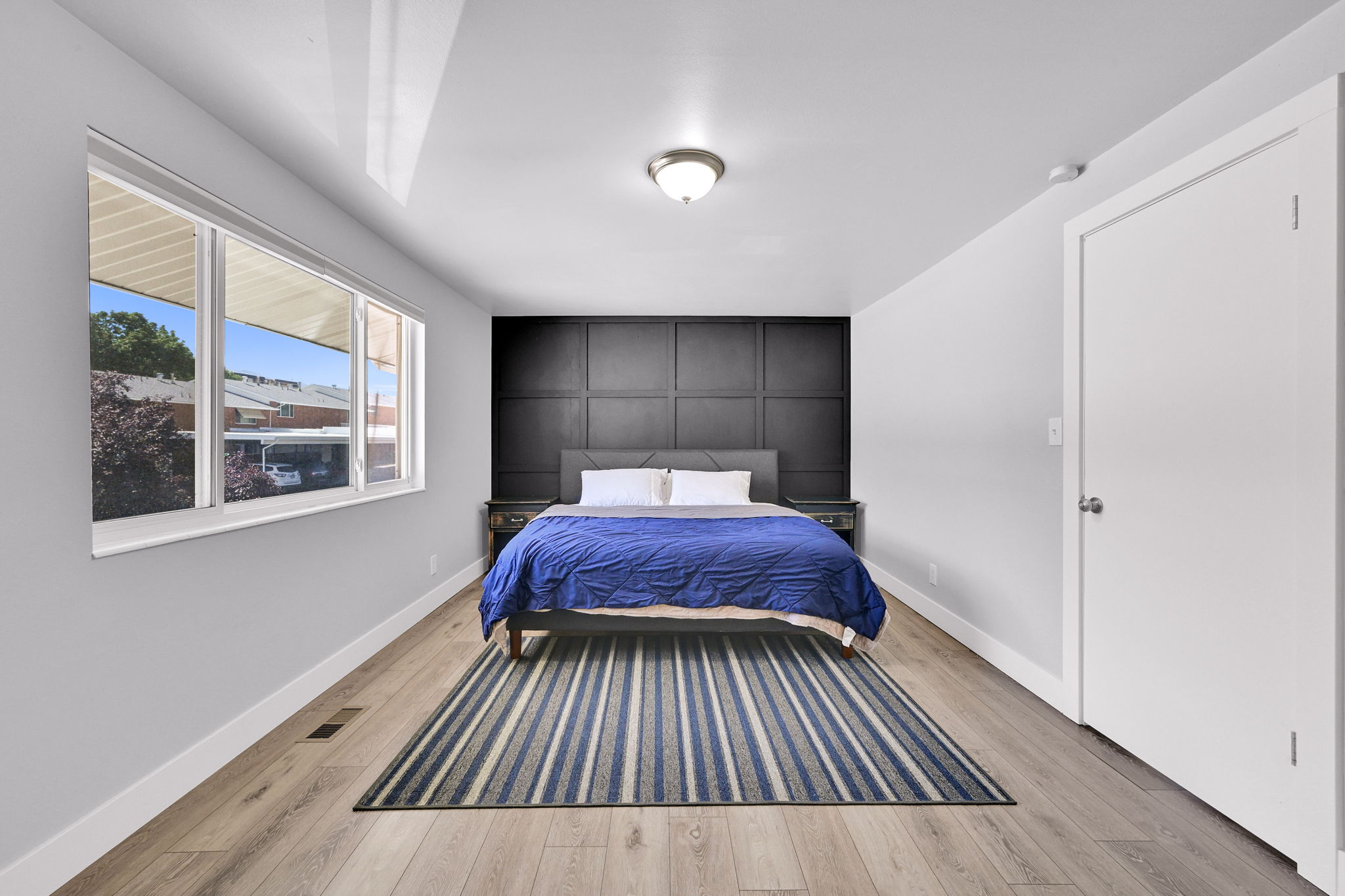 Bedroom featuring a paneled accent wall, wood-finish flooring, and white trim