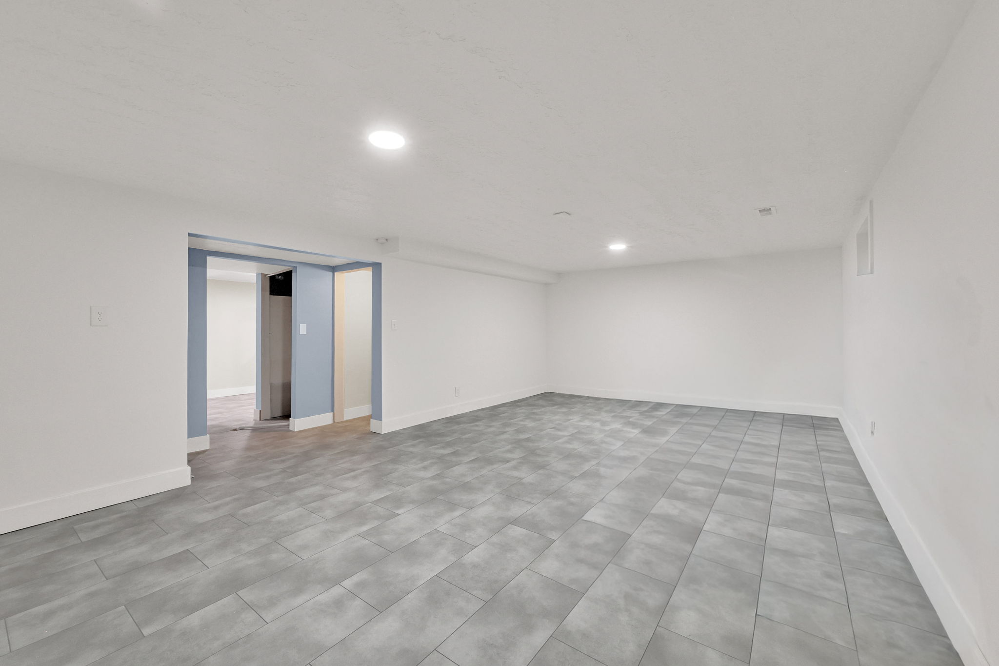 Spacious room featuring light gray tile flooring, white walls, and recessed lighting
