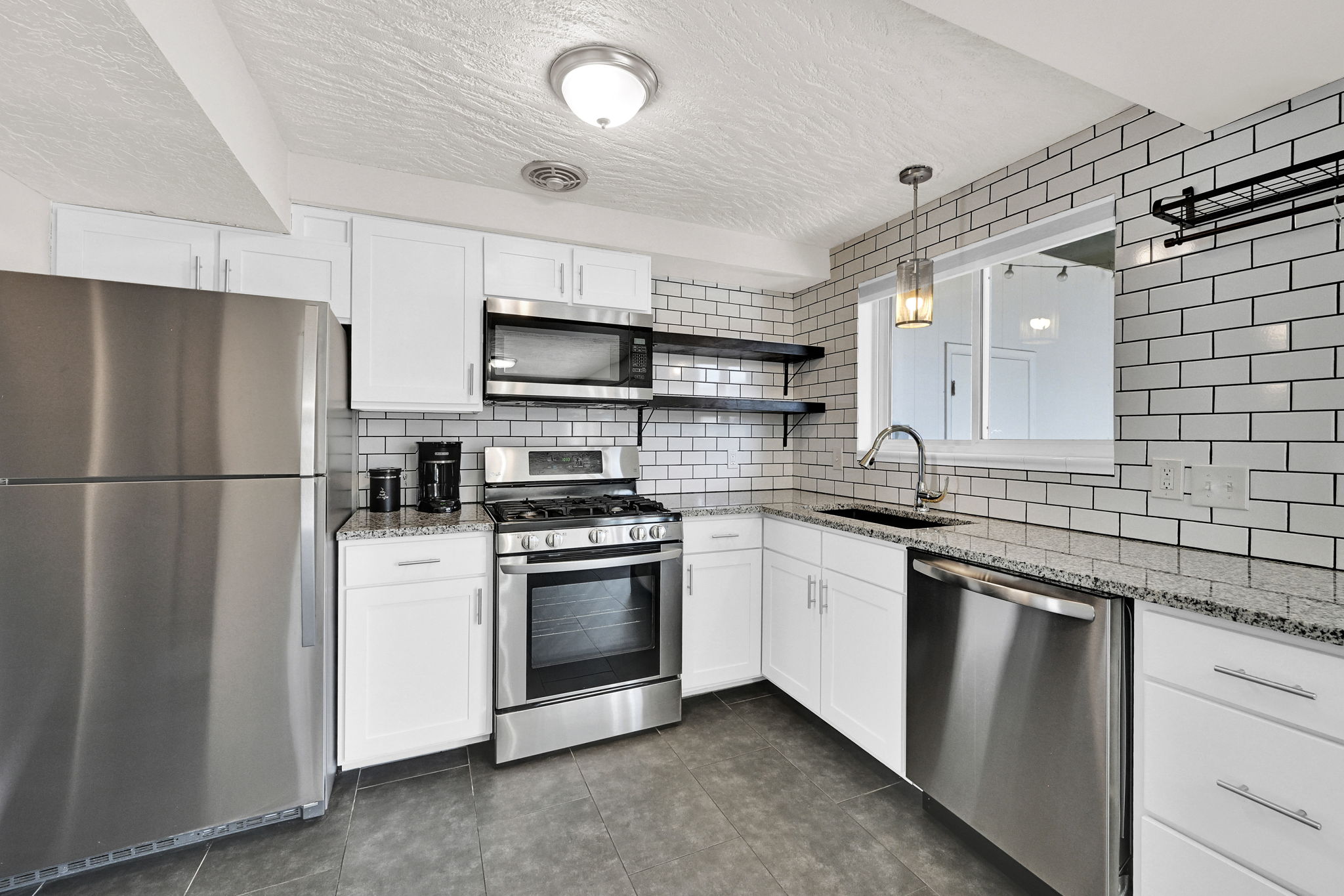 Modern kitchen featuring stainless steel appliances, white subway tile backsplash, white cabinetry with contemporary hardware, stone-finish countertops, and dark tile flooring