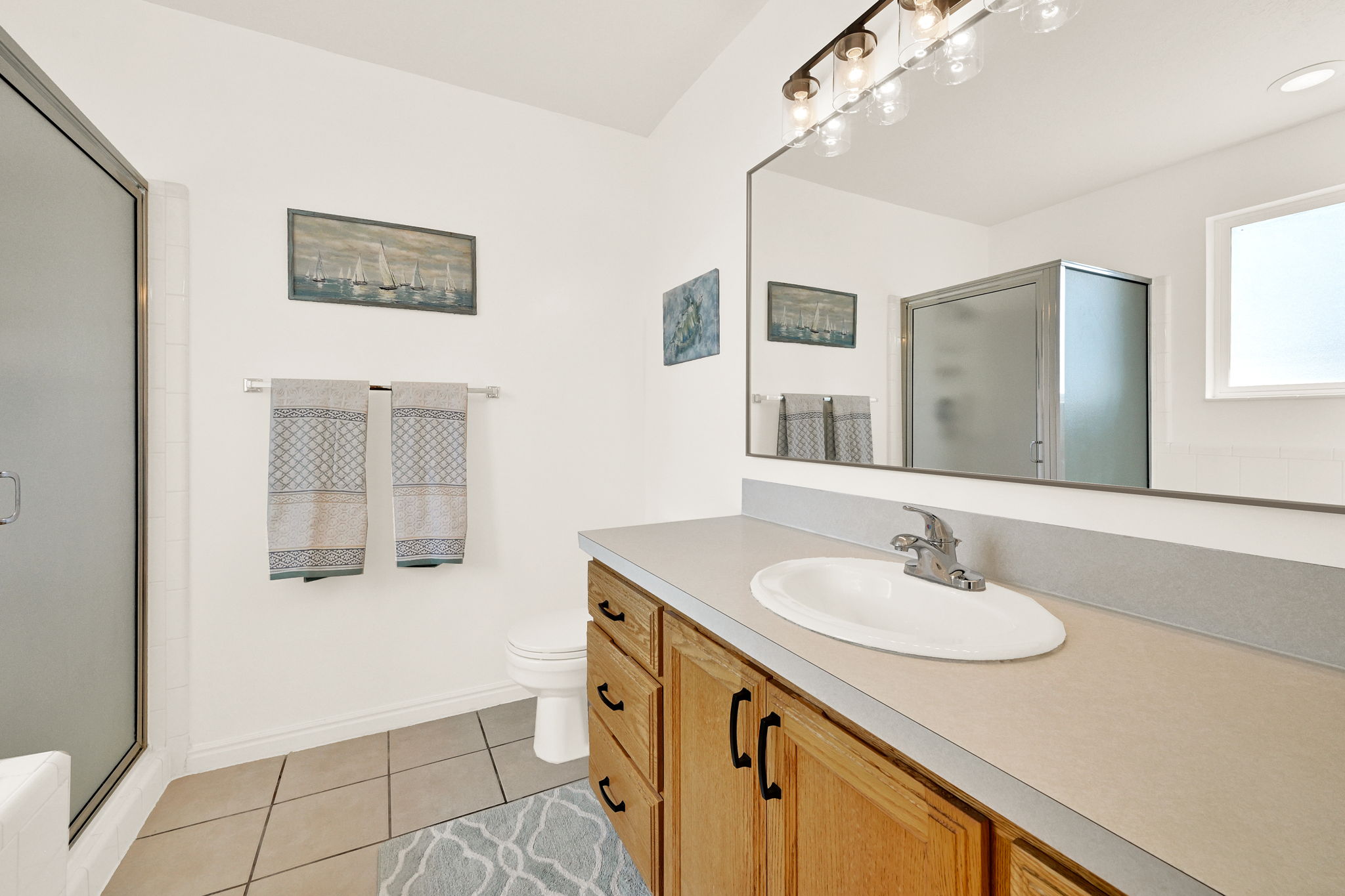 Bathroom featuring a wood-finish vanity with an integrated sink, a large mirror, and a frosted glass shower enclosure