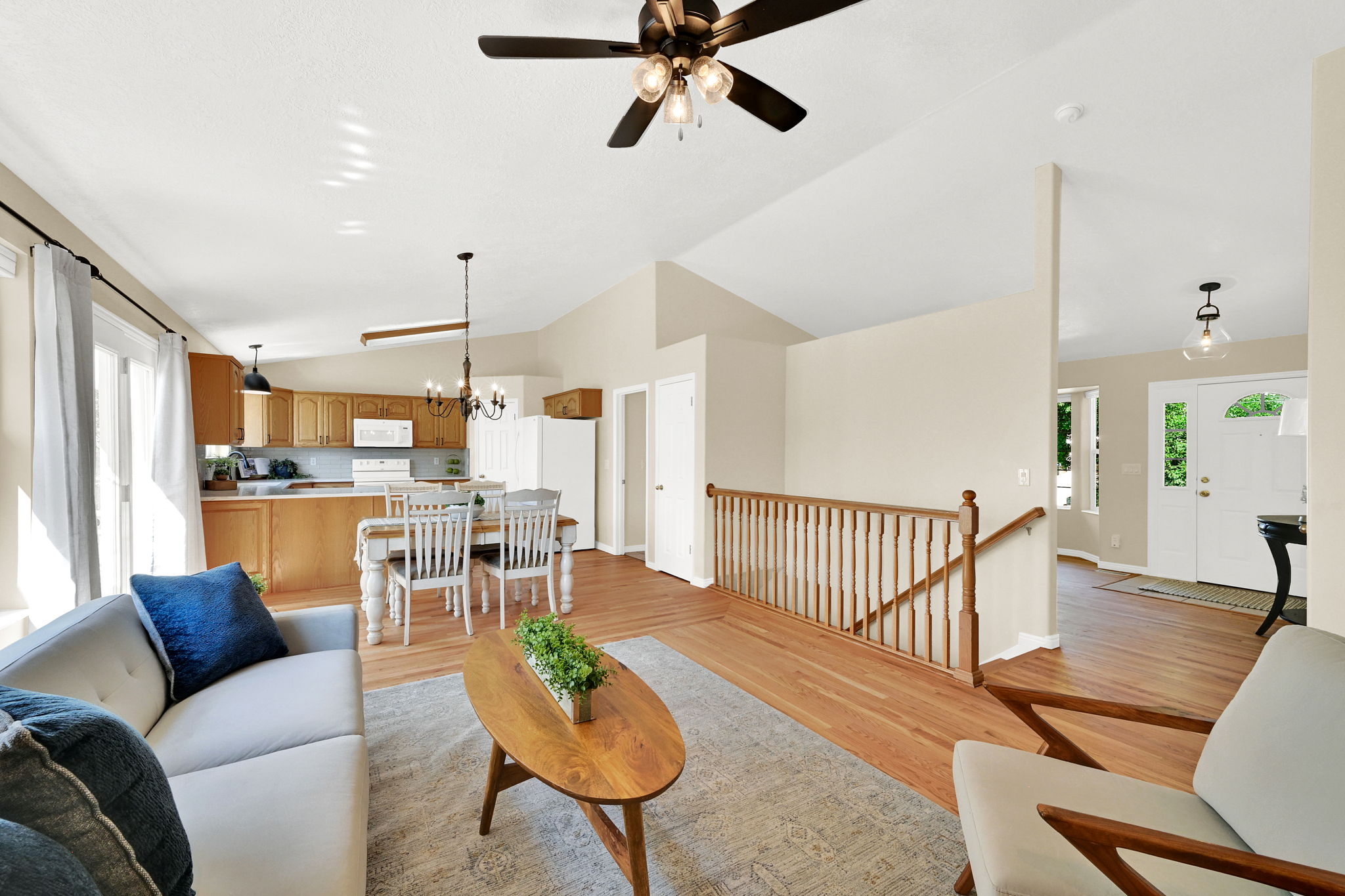Open concept living area featuring vaulted ceilings, hardwood flooring, a ceiling fan with integrated lighting, and a sliding glass door