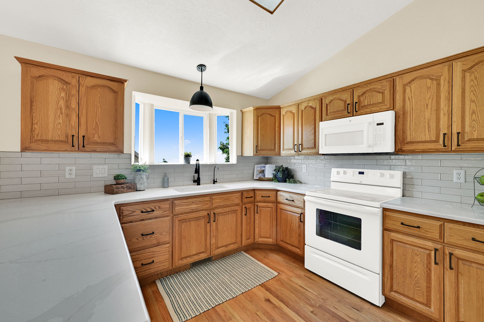 Expansive kitchen featuring wood-finish cabinetry, white countertops, subway tile backsplash, a bay window, and hardwood flooring