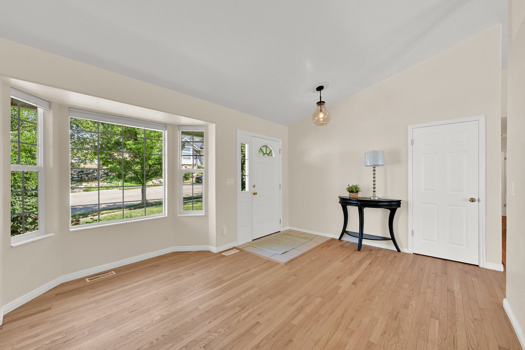 Bright entry area featuring a bay window, wood-finish flooring, and vaulted ceiling
