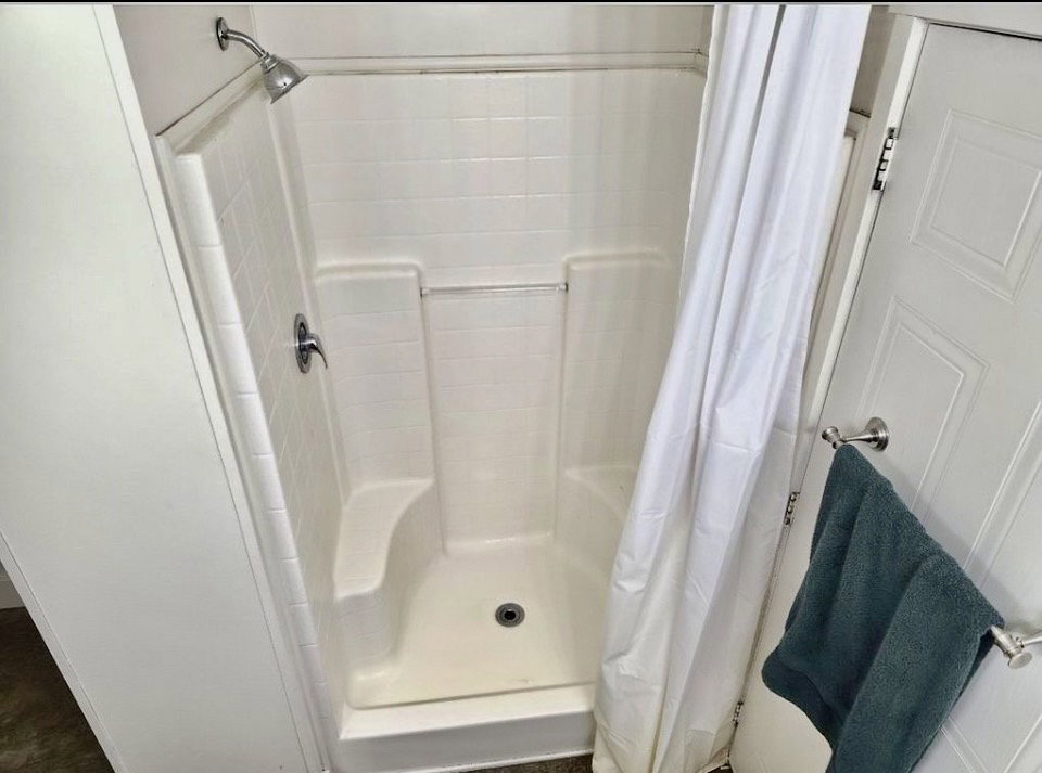 White shower stall featuring an integrated bench and chrome fixtures