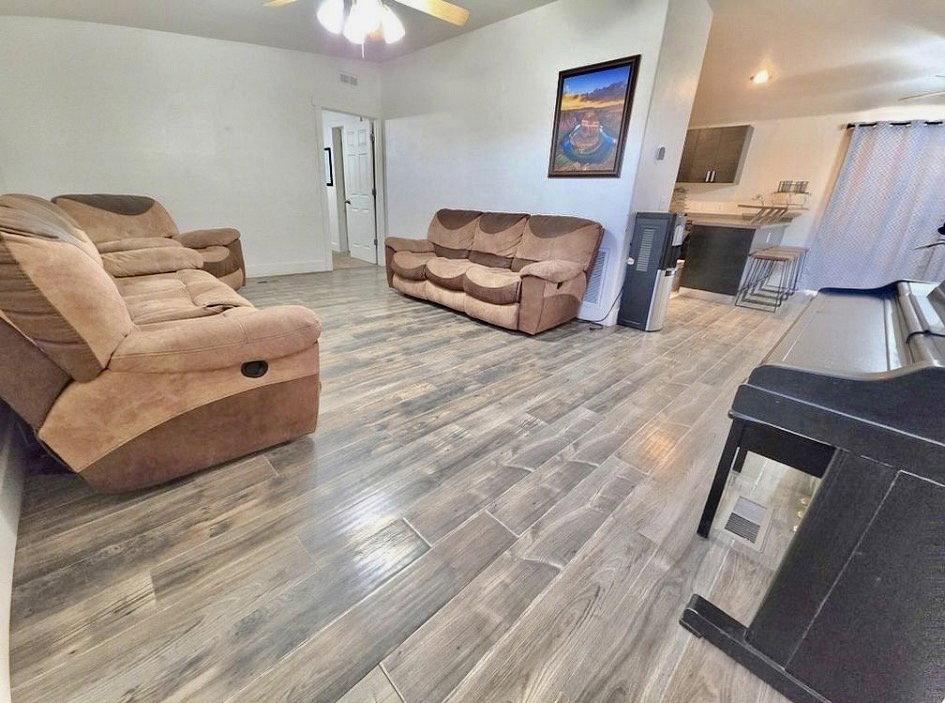 Spacious living area featuring wood-finish flooring, a ceiling fan, and white walls