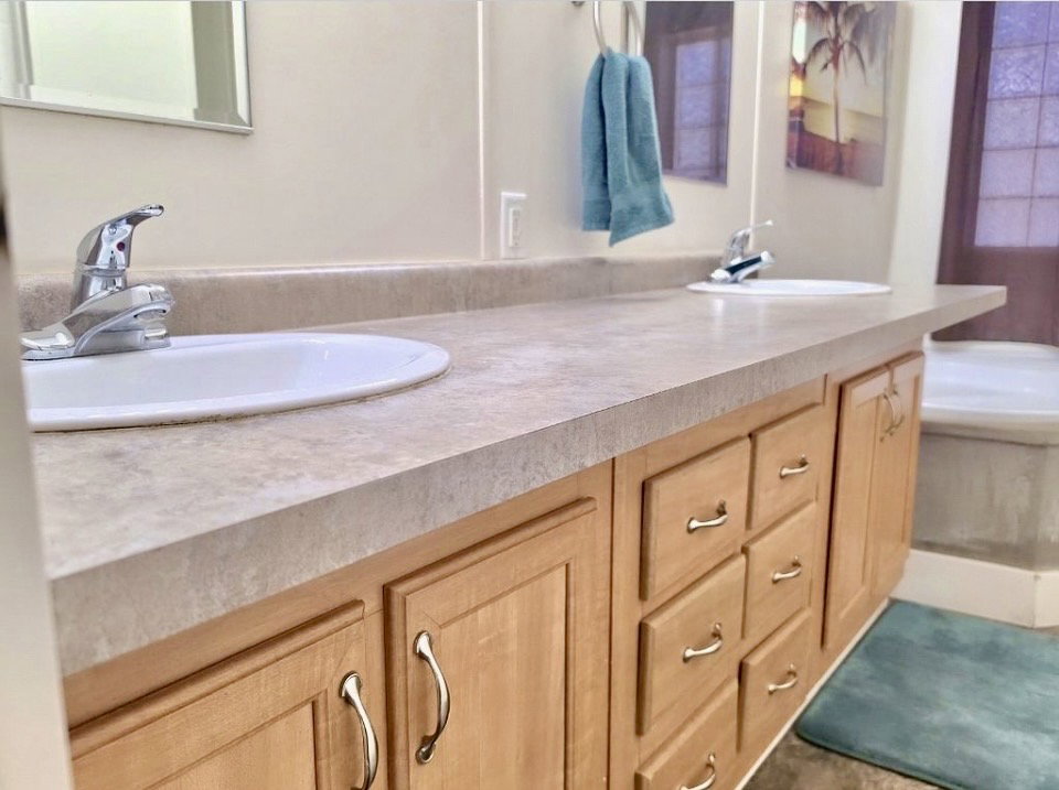 Double vanity with two integrated sinks, light-toned countertop, and natural wood cabinetry featuring brushed nickel hardware