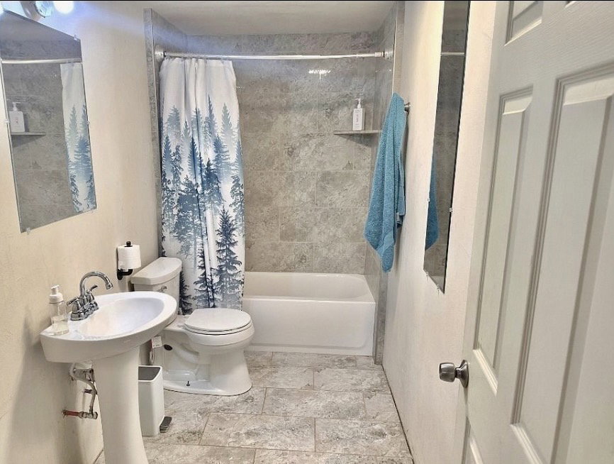 Bathroom featuring a pedestal sink, white toilet, and a bathtub with a tiled surround