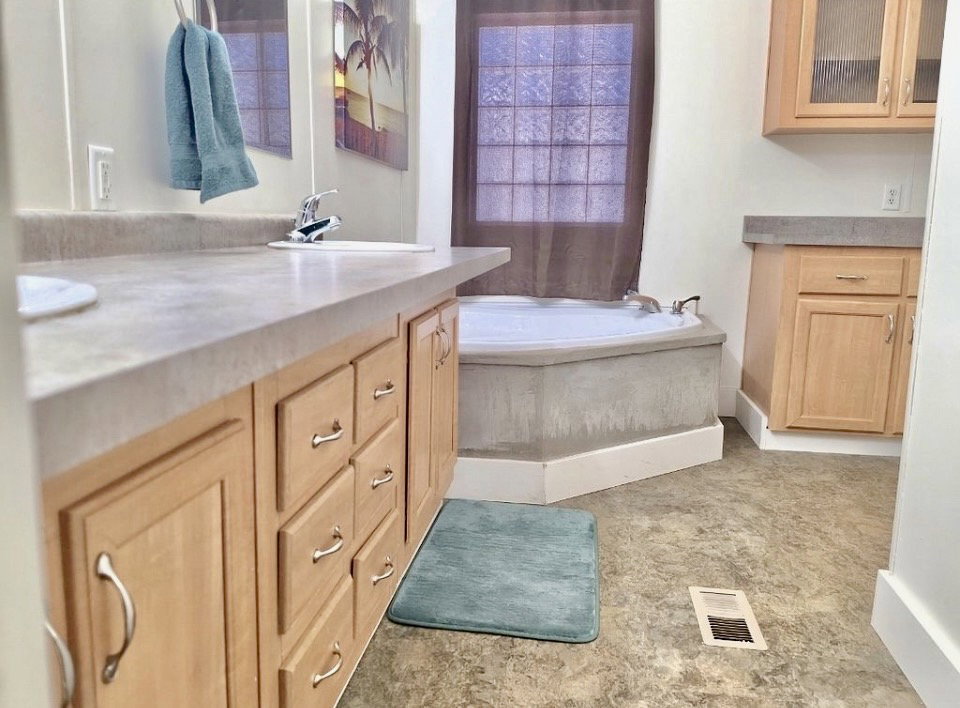 Bathroom featuring a built-in corner tub, light wood-finish cabinetry, a single vanity with an integrated sink, a tiled floor, and a window with privacy glass
