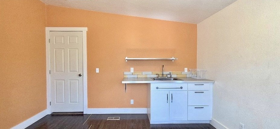 Compact kitchenette featuring white cabinetry, a stainless steel sink, and a tiled backsplash