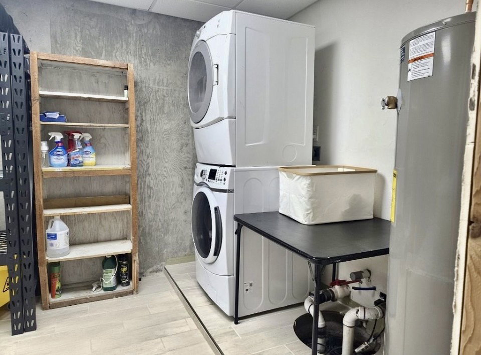 Dedicated utility area featuring a stacked washer and dryer unit, light-toned tile flooring, and a water heater