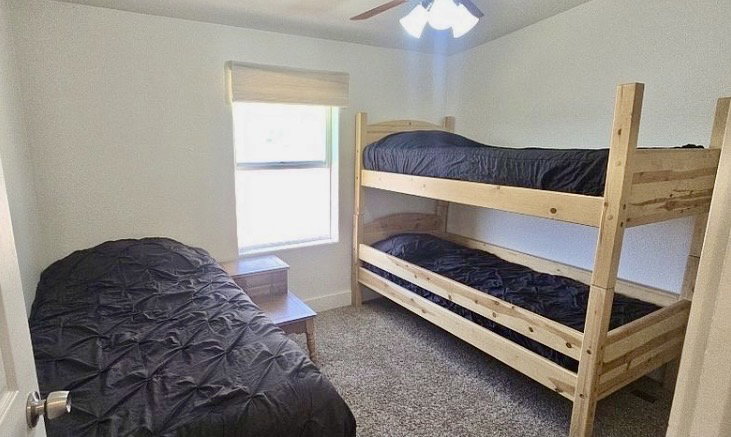 Carpeted room featuring a window with a roller shade, a ceiling fan with integrated lighting, and white painted walls
