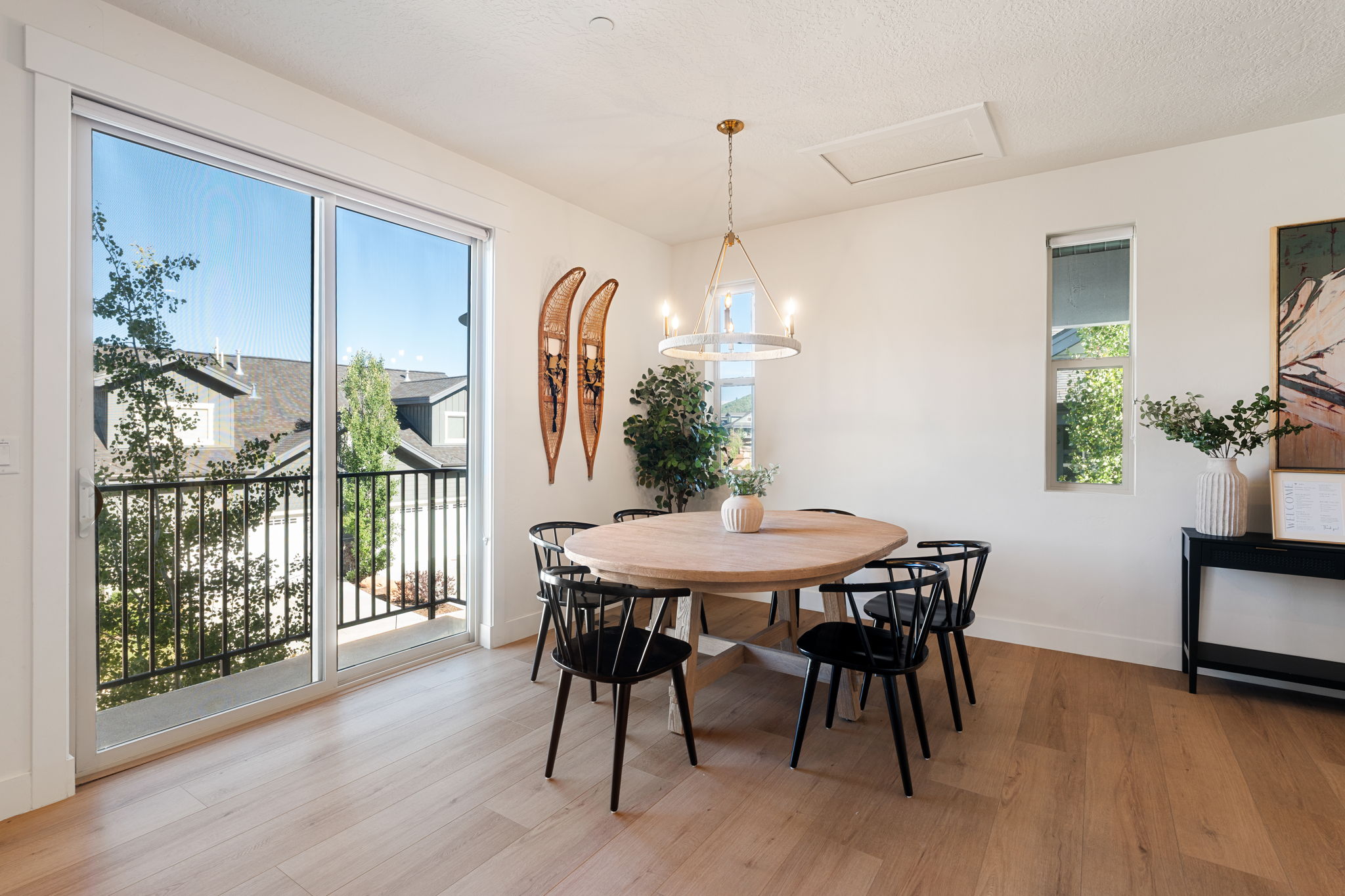 Interior space featuring wood-finish flooring, a large sliding glass door opening to a black iron railing, a single vertical window, and a modern chandelier light fixture