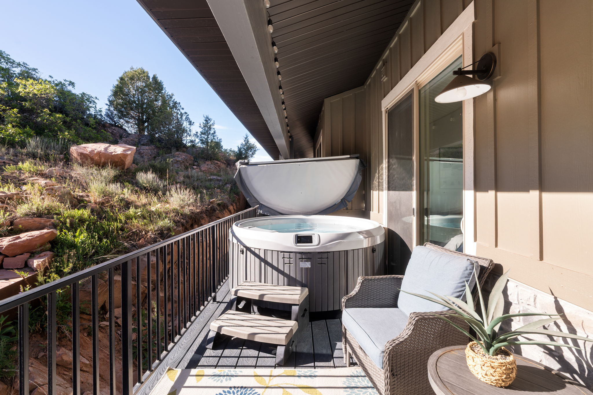 Deck featuring a built-in hot tub with cover, composite decking, black metal railing, and a sliding glass door