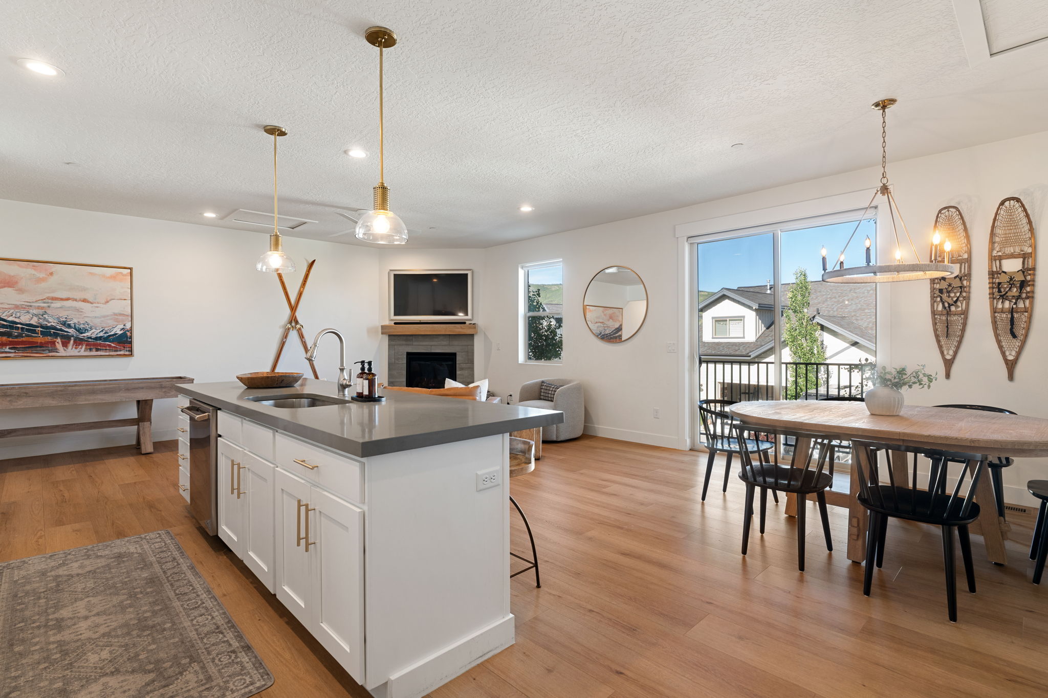 Open-concept living space featuring wood-finish flooring, a kitchen island with a sink and pendant lighting, a built-in fireplace, and a sliding glass door opening to an exterior balcony