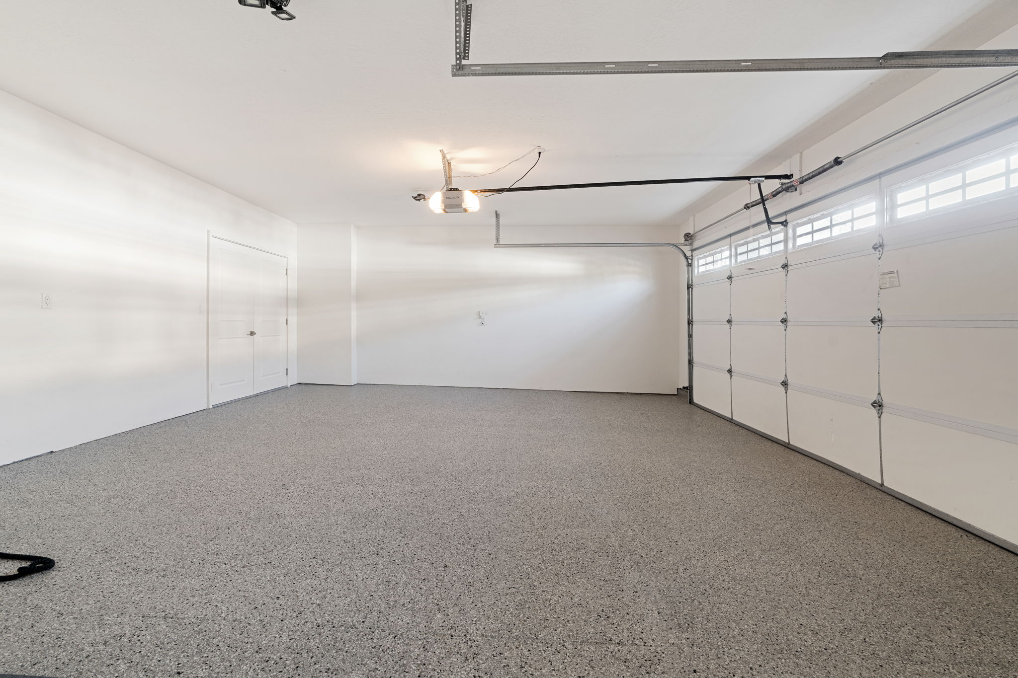 Spacious garage featuring a durable epoxy-coated floor, bright white walls, and a sectional garage door with upper window panels