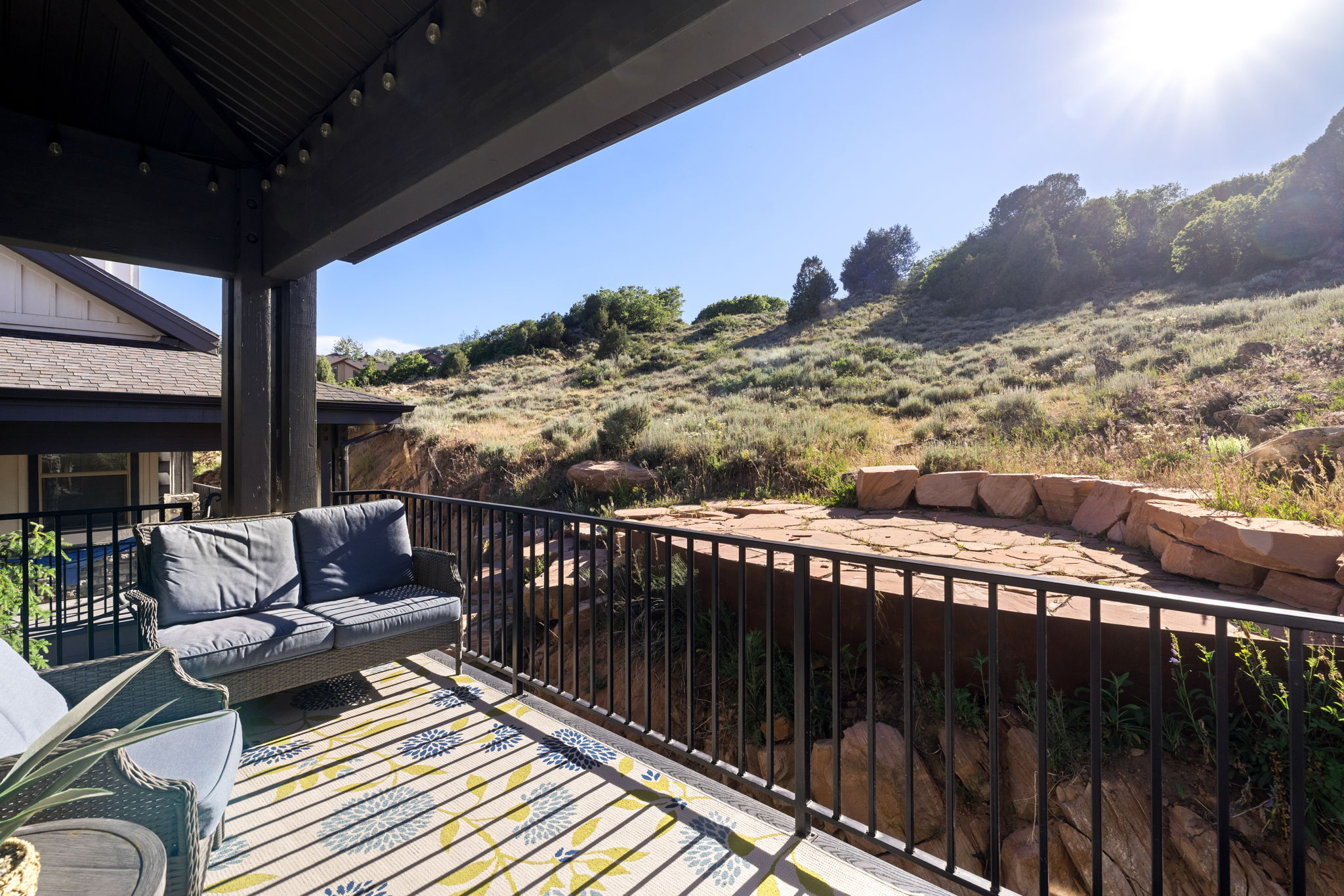 Covered outdoor patio with a black metal railing and string lighting