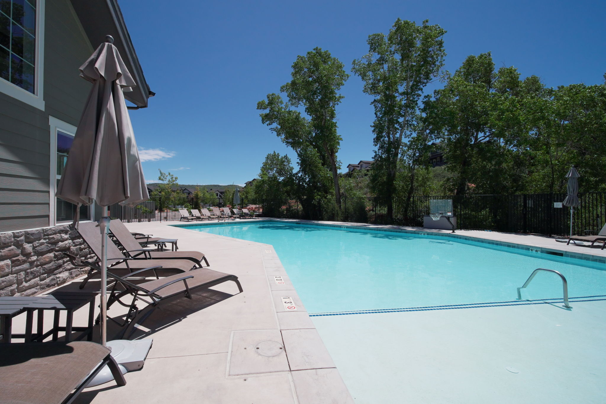 Outdoor swimming pool with concrete decking, surrounding lounge chairs, and an integrated umbrella