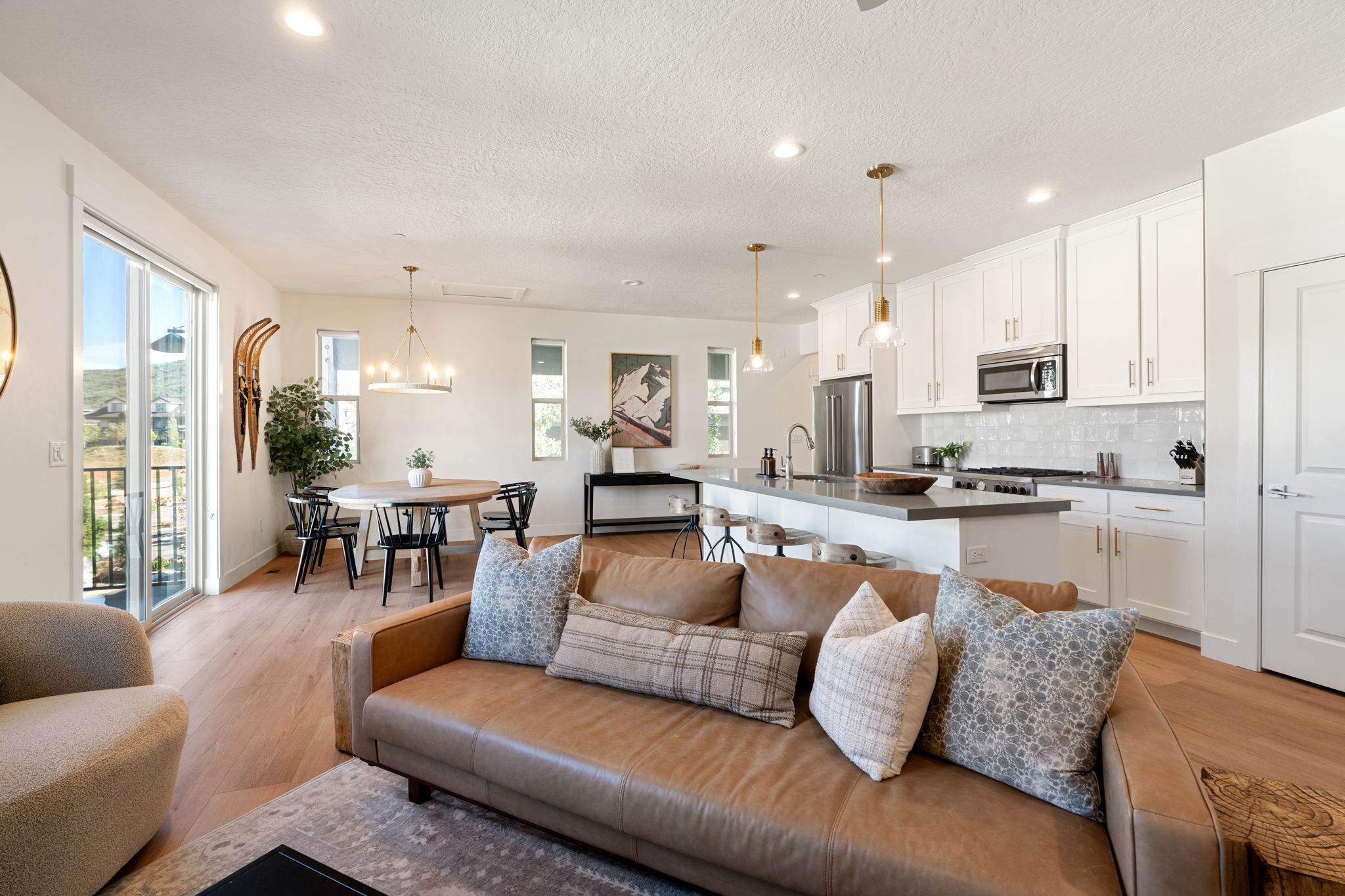 Open-concept living area featuring a kitchen with white cabinetry and stainless steel appliances, a dining area with a modern chandelier, and wood-finish flooring