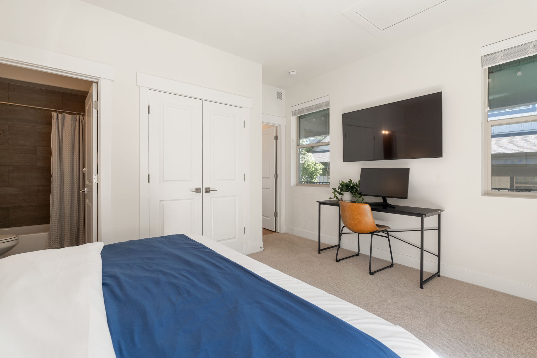 Carpeted bedroom featuring white walls, two windows with blinds, and white double-panel doors