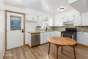 Bright kitchen featuring wood-finish flooring, white cabinetry, stainless steel dishwasher, and a black gas range