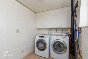 Laundry area featuring white cabinetry, light-toned walls, plumbing infrastructure, and a ceiling-mounted light fixture