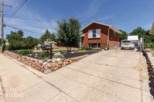 Brick exterior residence featuring white window shutters, a stone-lined planter with dark mulch, mature landscaping, and an extended concrete driveway