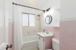 Bathroom featuring a white bathtub, pink tiled walls, white vanity with integrated sink, and an overhead light fixture