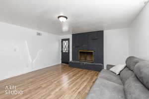 Living area featuring a painted brick fireplace, a dark entry door with decorative glass inserts, and wood-finish flooring