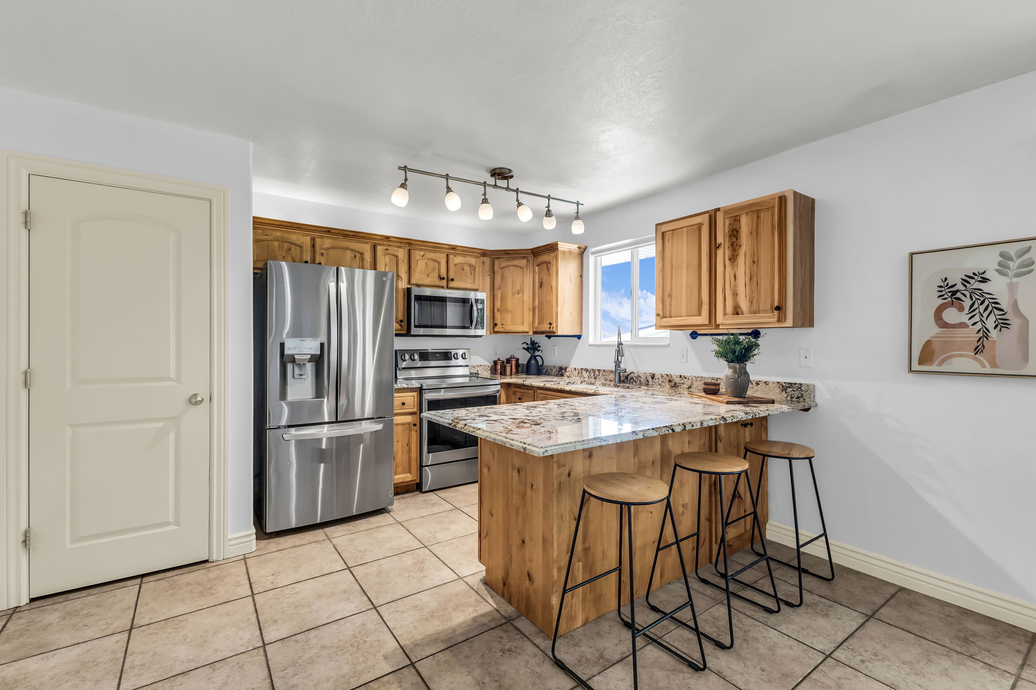 Kitchen featuring stainless steel appliances, wood cabinetry, stone countertops, and tile flooring