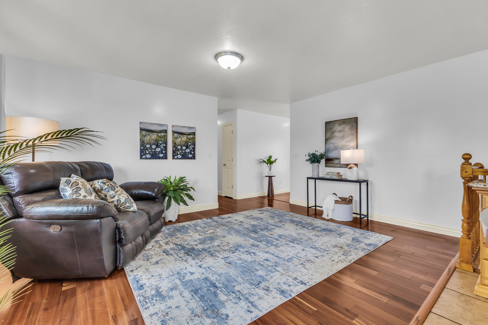 Spacious living area featuring rich wood-finish flooring, white wall finishes, and a contemporary flush-mount ceiling light fixture