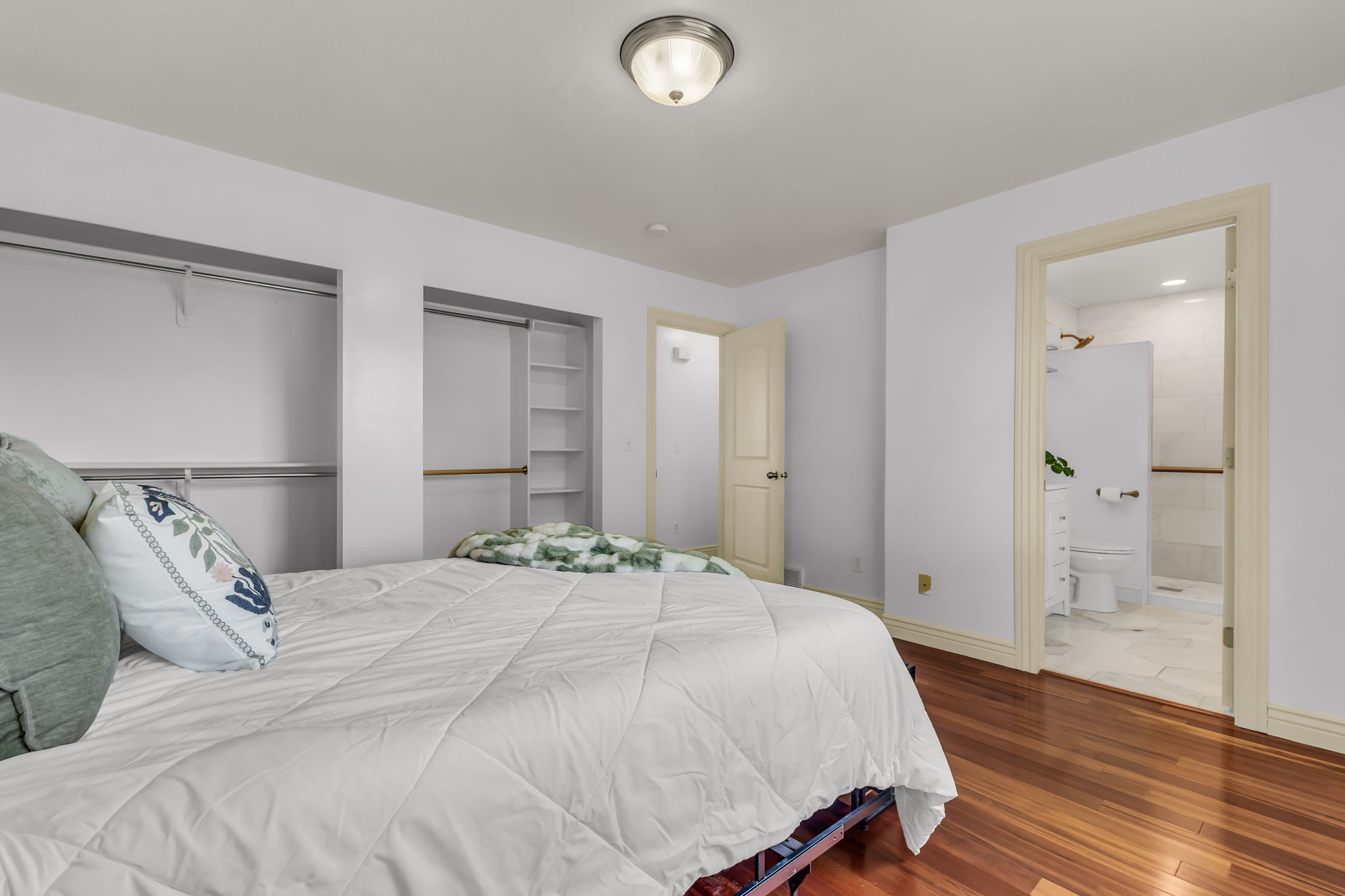Bedroom featuring polished wood-finish flooring, two open closet spaces with hanging rods and shelving, and a neutral wall color