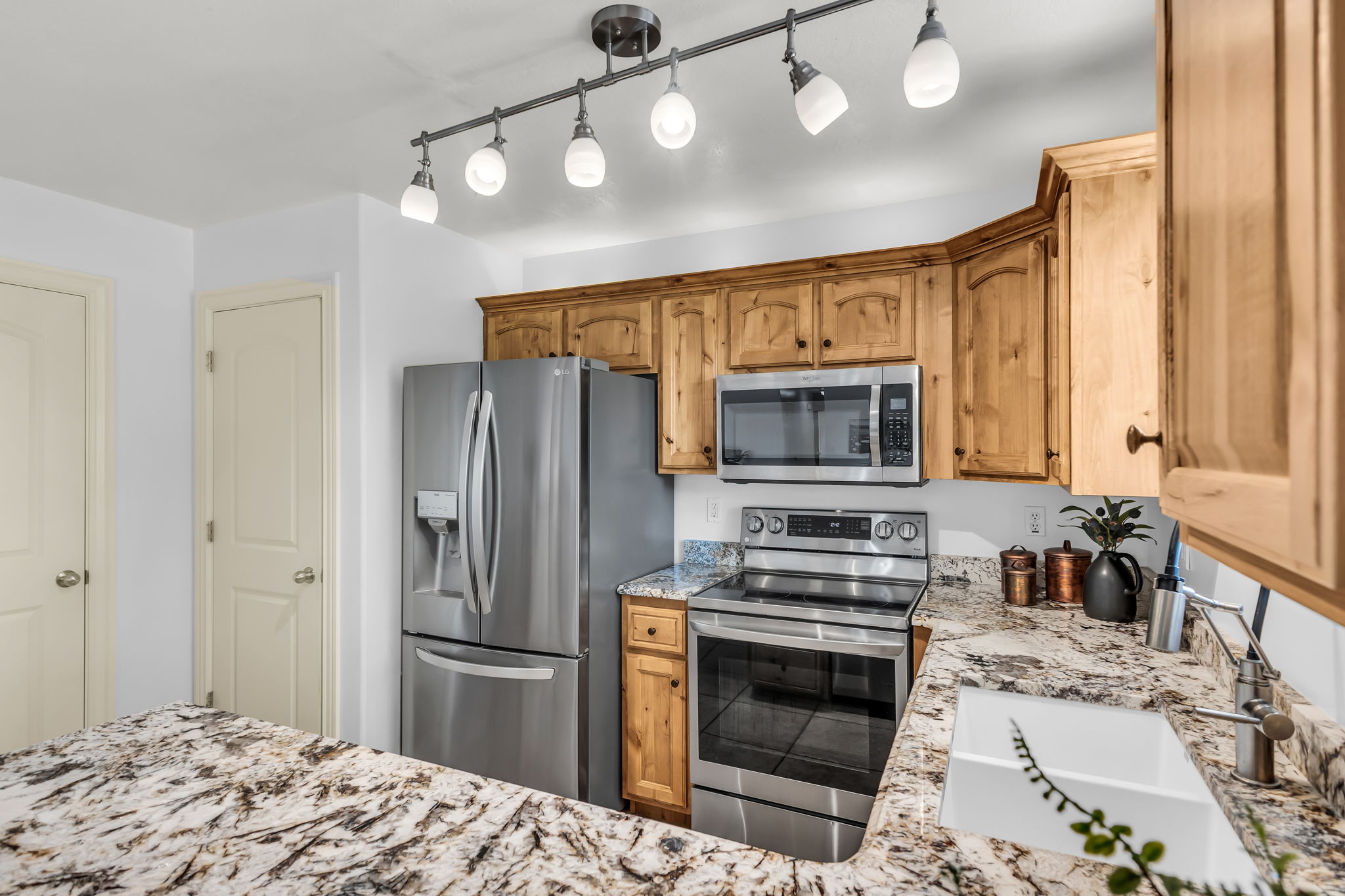 Kitchen featuring granite countertops, wood cabinetry, stainless steel appliances, and a white sink with a brushed nickel faucet