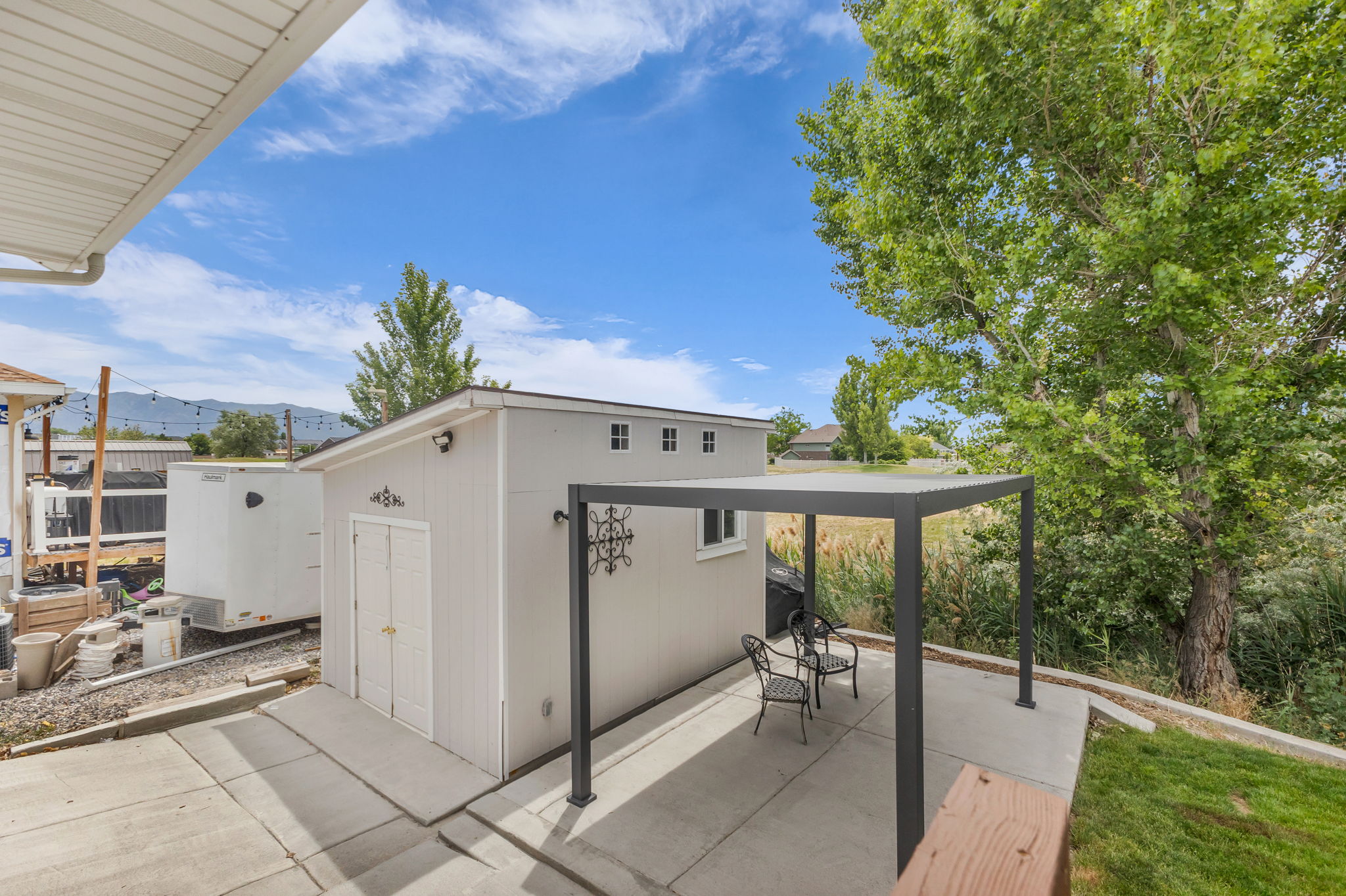 Detached storage shed with double doors and transom windows, featuring an adjacent paved patio with a modern pergola