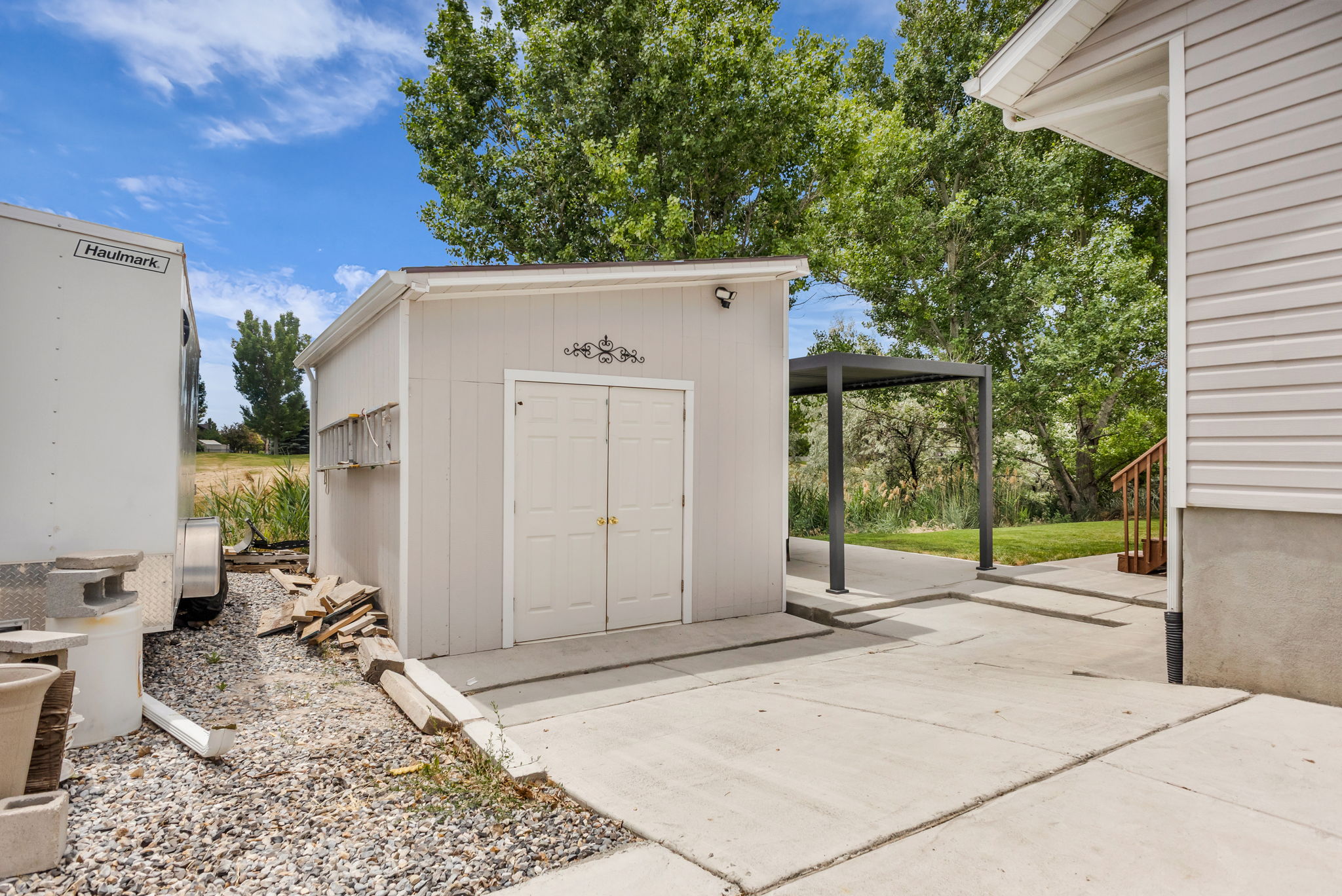 Detached storage shed with double doors, concrete pad, and covered outdoor structure