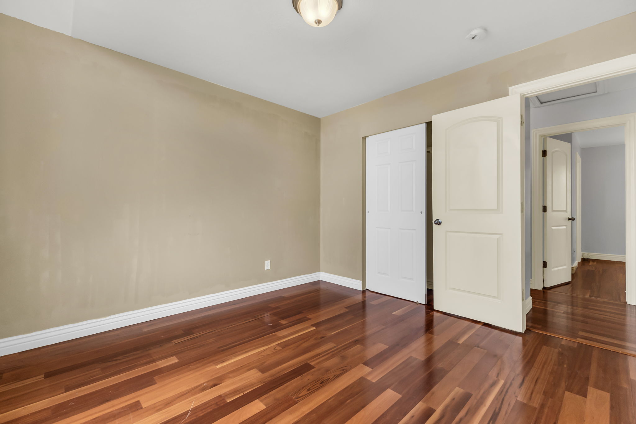 Room featuring polished wood-finish flooring, neutral-toned walls, white baseboards, and a semi-flush ceiling light fixture