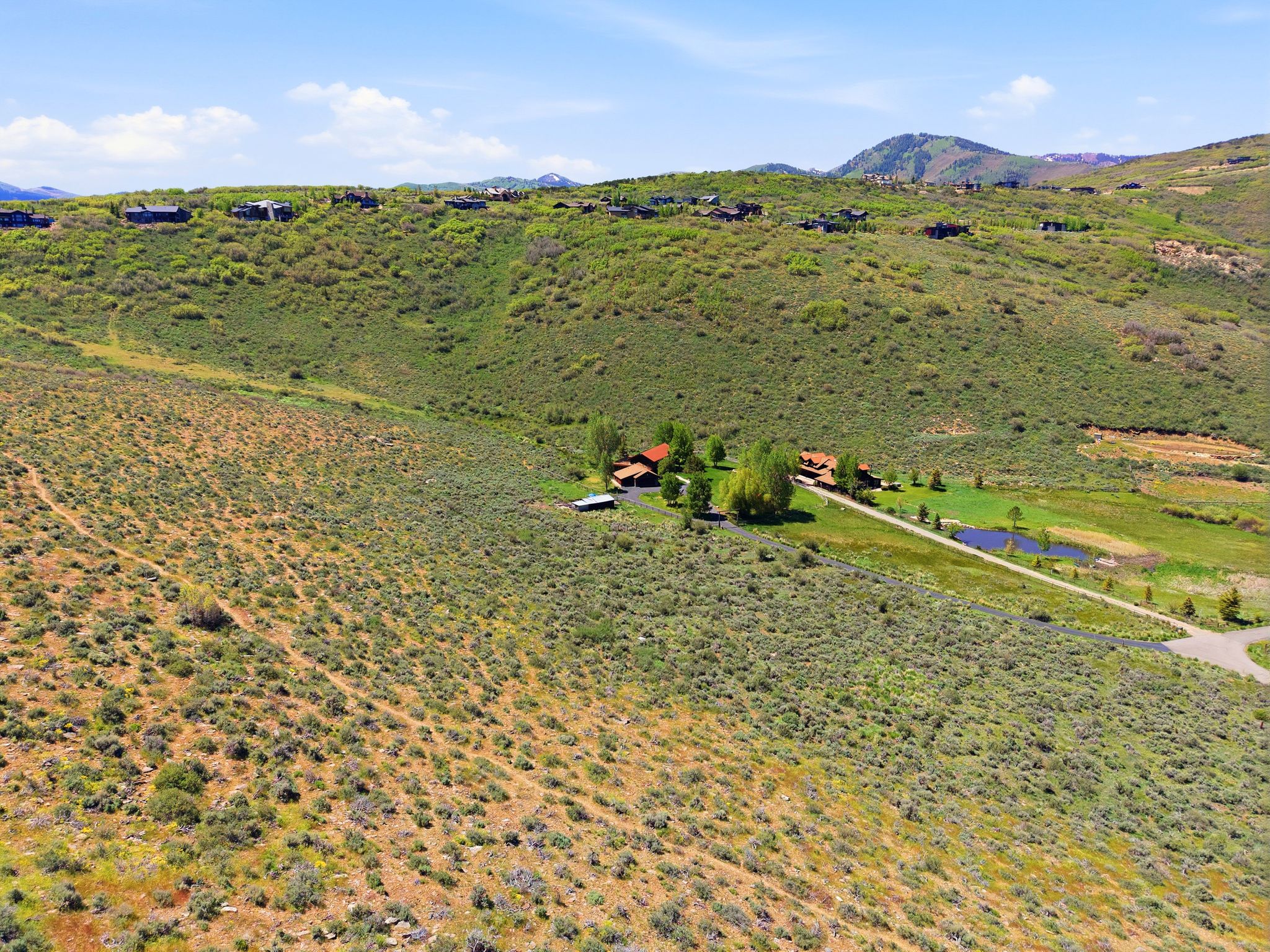 Expansive natural landscape featuring a private residence, additional outbuildings, a visible pond, and a long driveway