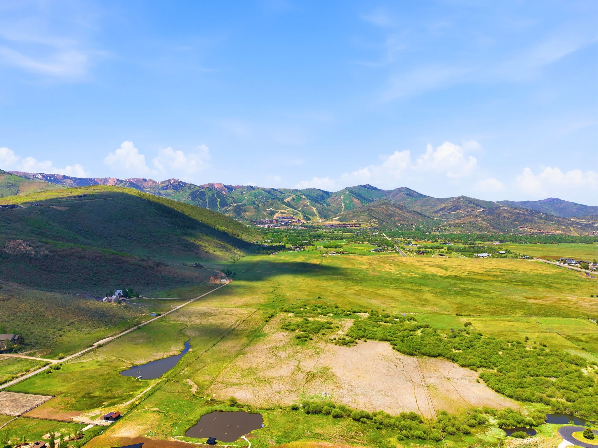 Expansive green landscape with distant mountains, two visible ponds, and scattered structures