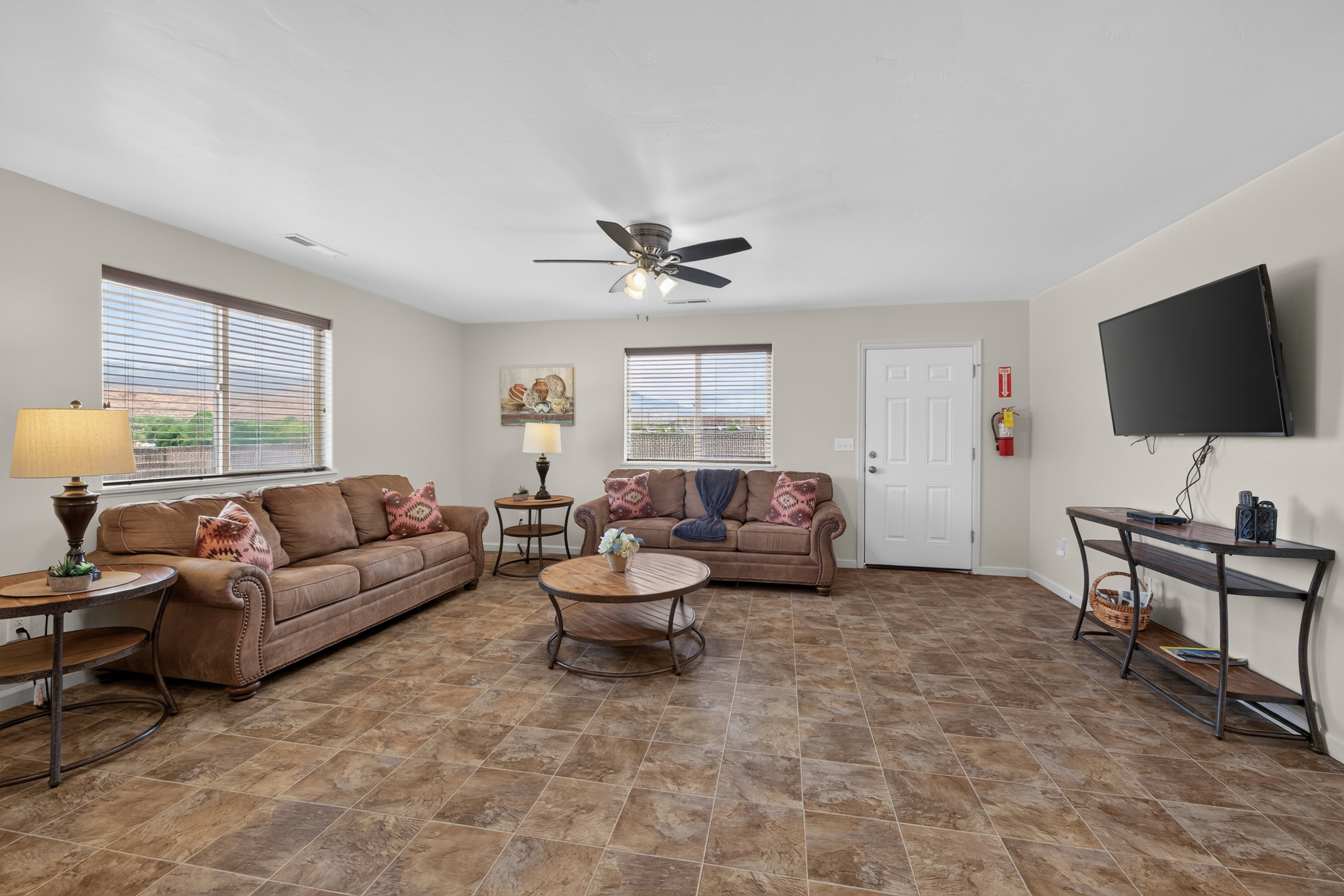 Spacious living area featuring multi-toned tile flooring, neutral wall paint, and multiple windows with horizontal blinds