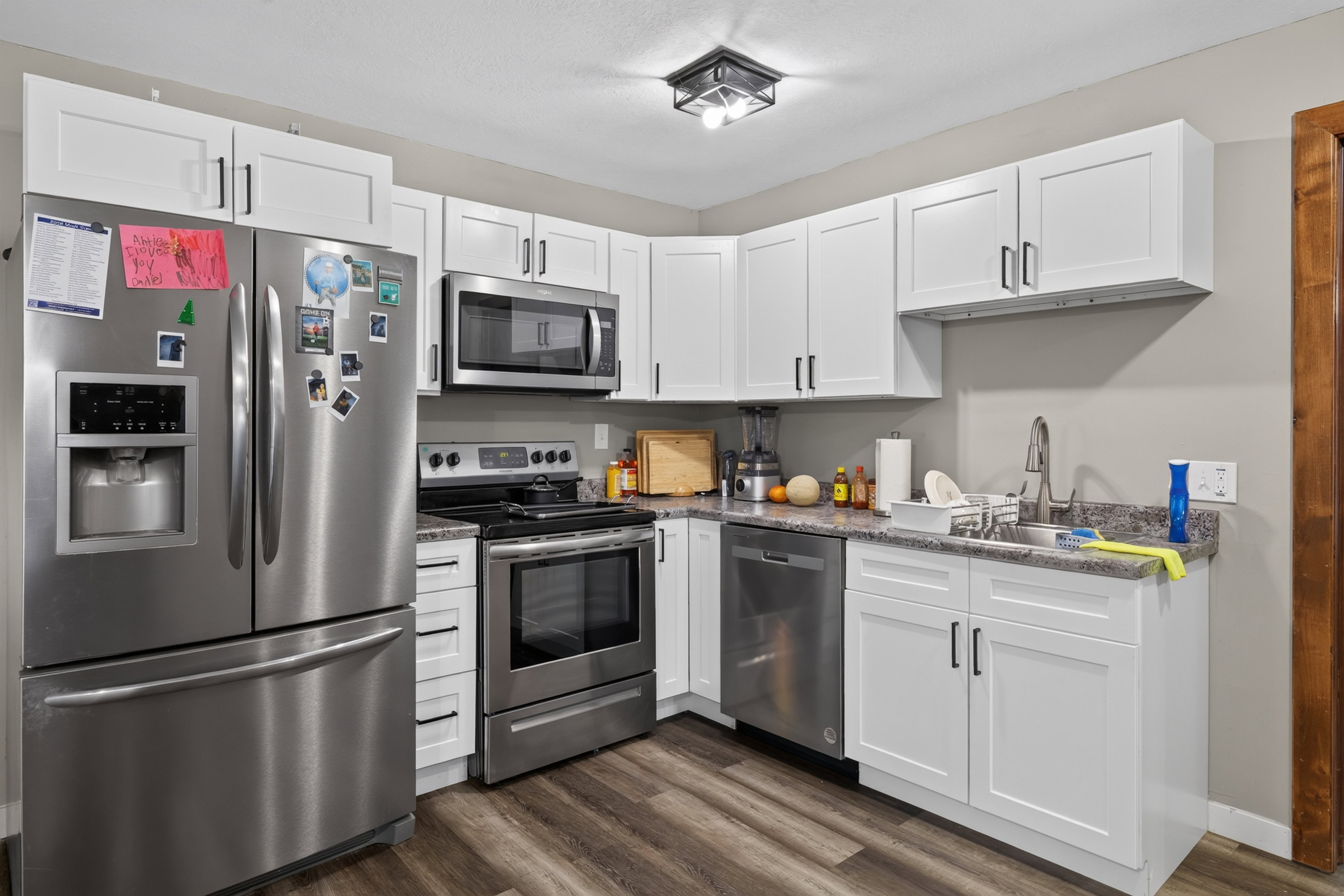 Kitchen featuring white shaker-style cabinetry, stainless steel appliances, granite-look countertops, and wood-finish flooring