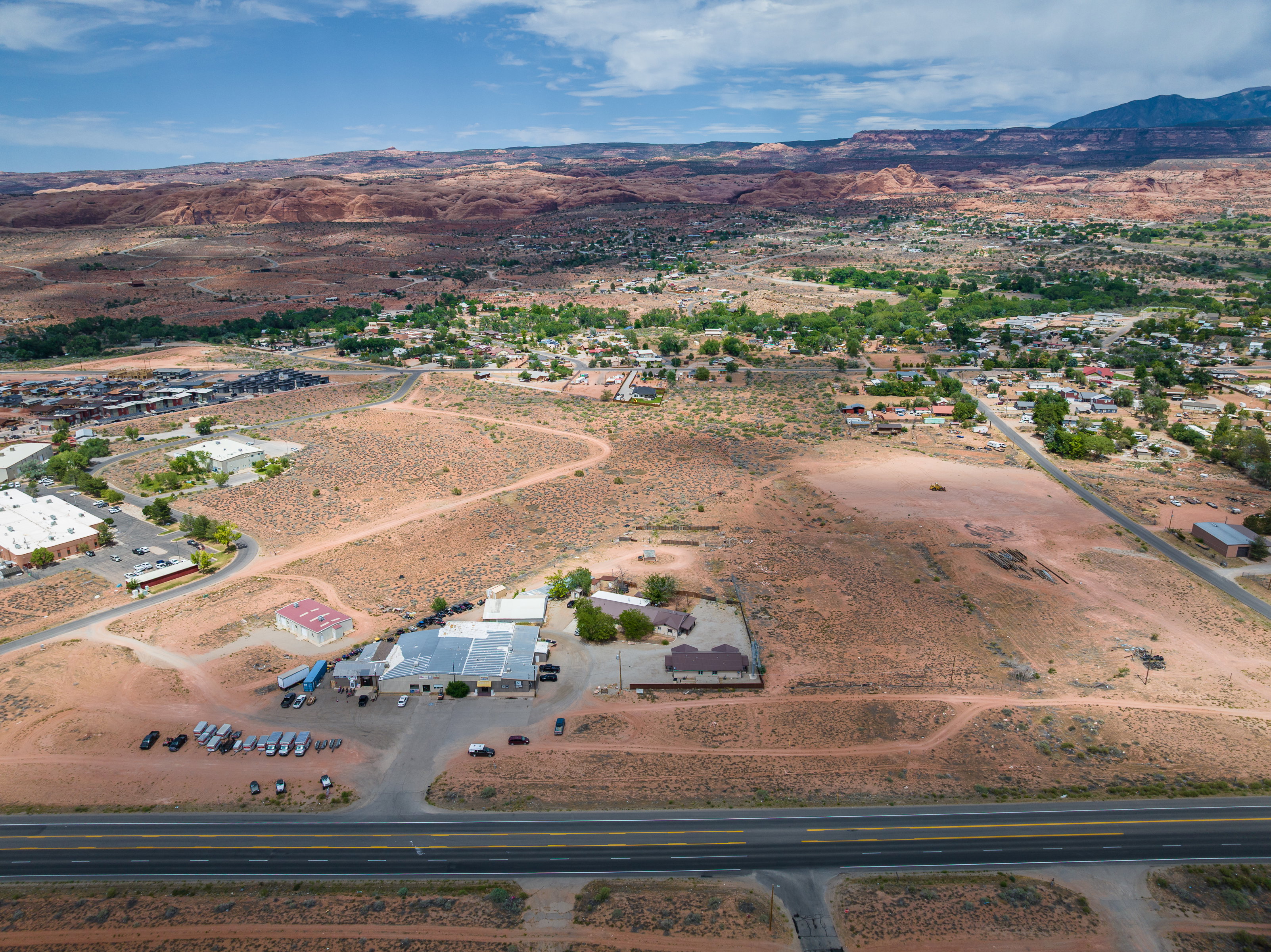 Expansive arid landscape featuring scattered buildings, a prominent multi-lane roadway, and distant mountain formations