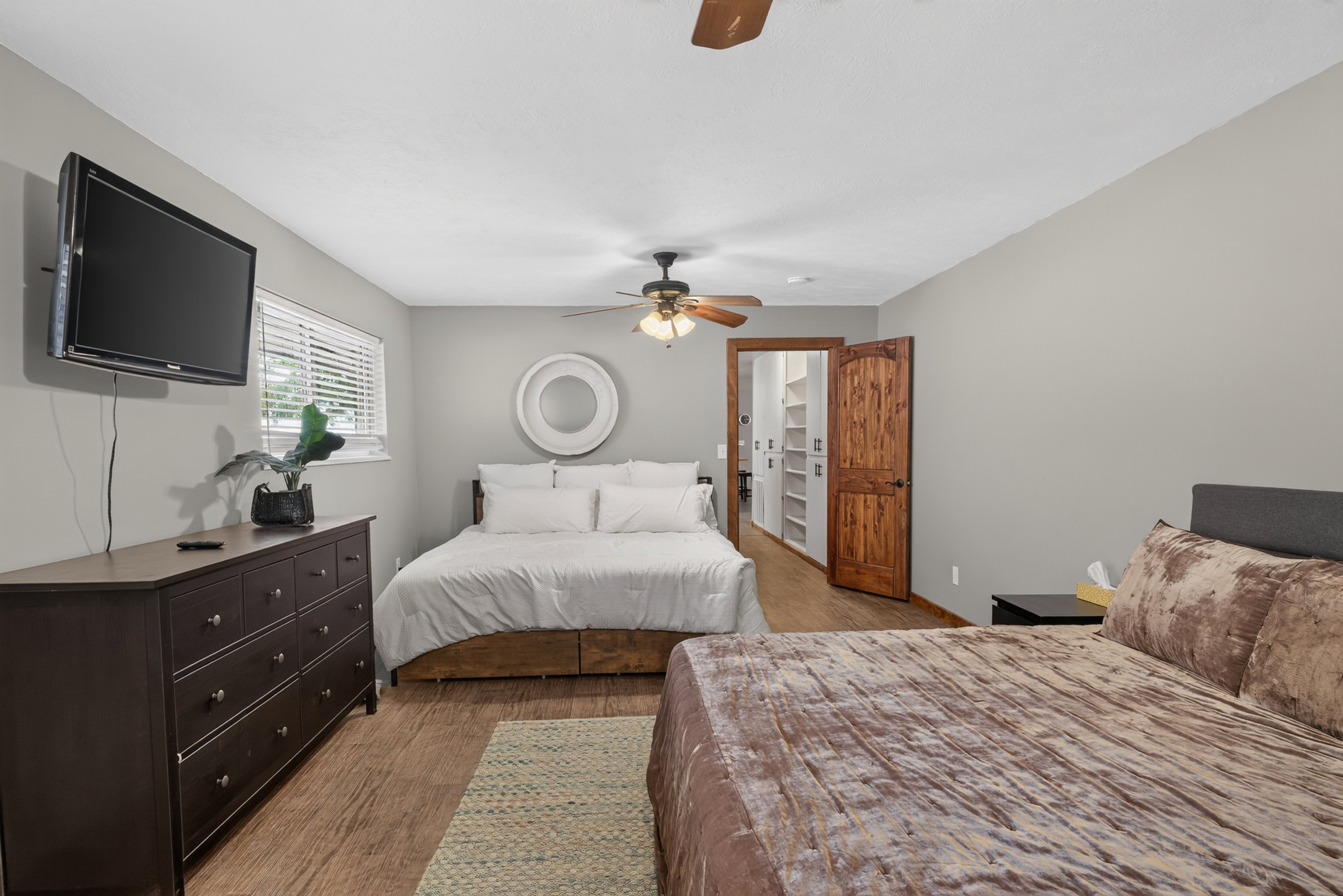 Bedroom featuring wood-finish flooring, a ceiling fan, window with blinds, and a closet with custom shelving and a wood door