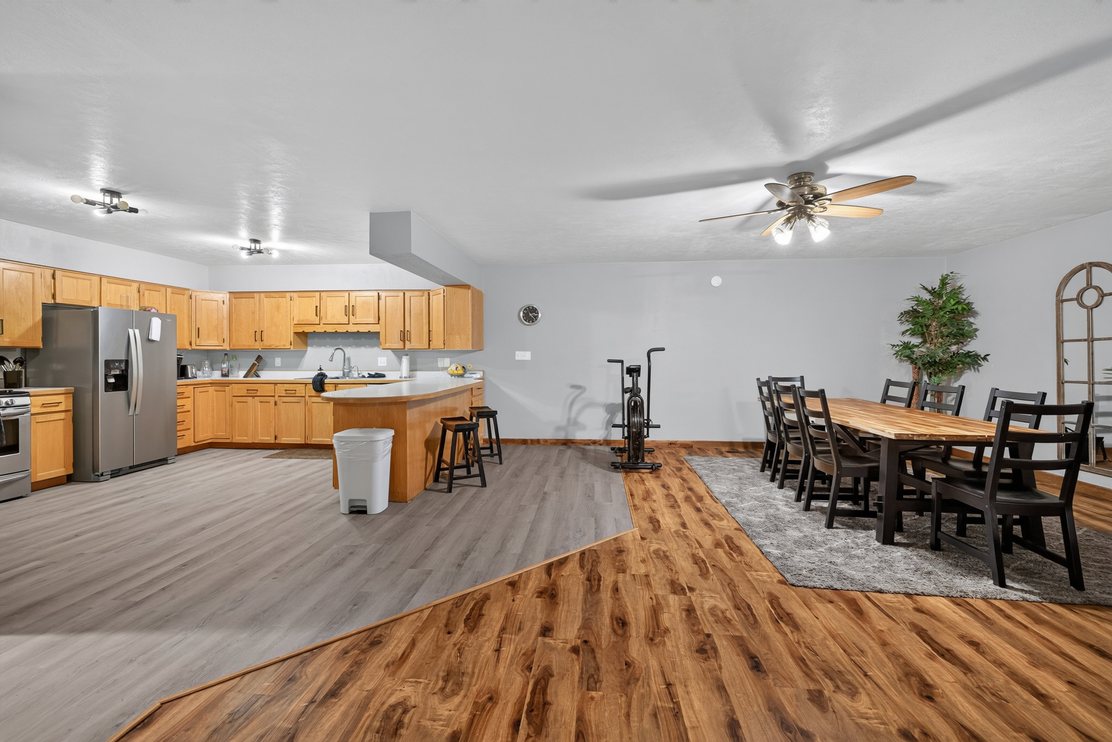 Open-concept kitchen and dining area featuring light wood cabinetry, a curved breakfast bar, stainless steel appliances, and contrasting wood-finish flooring