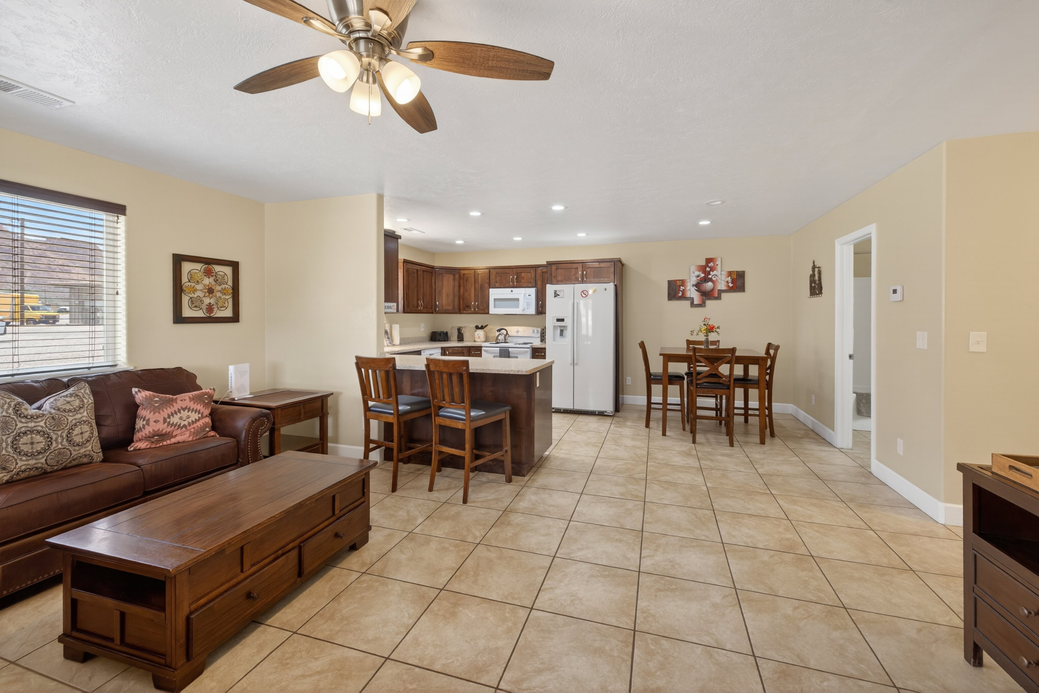 Open-concept living area featuring tile flooring, a ceiling fan, and a kitchen with dark wood-finish cabinetry, light countertops, and a breakfast bar