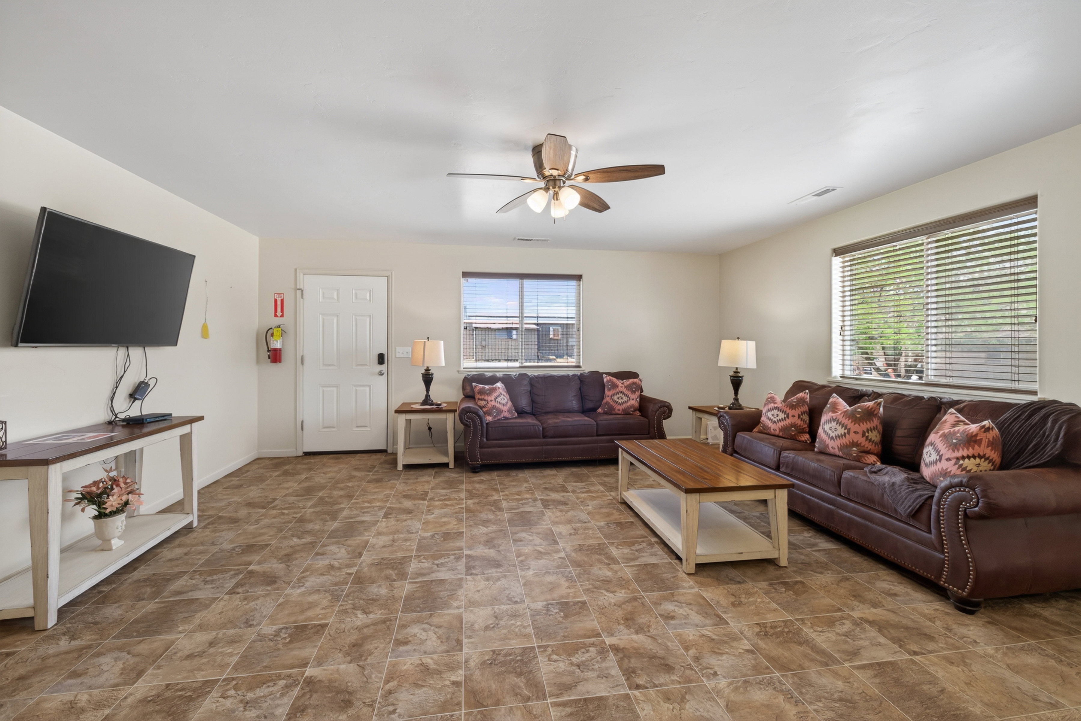 Spacious living area featuring neutral wall tones, tile flooring, and a ceiling fan