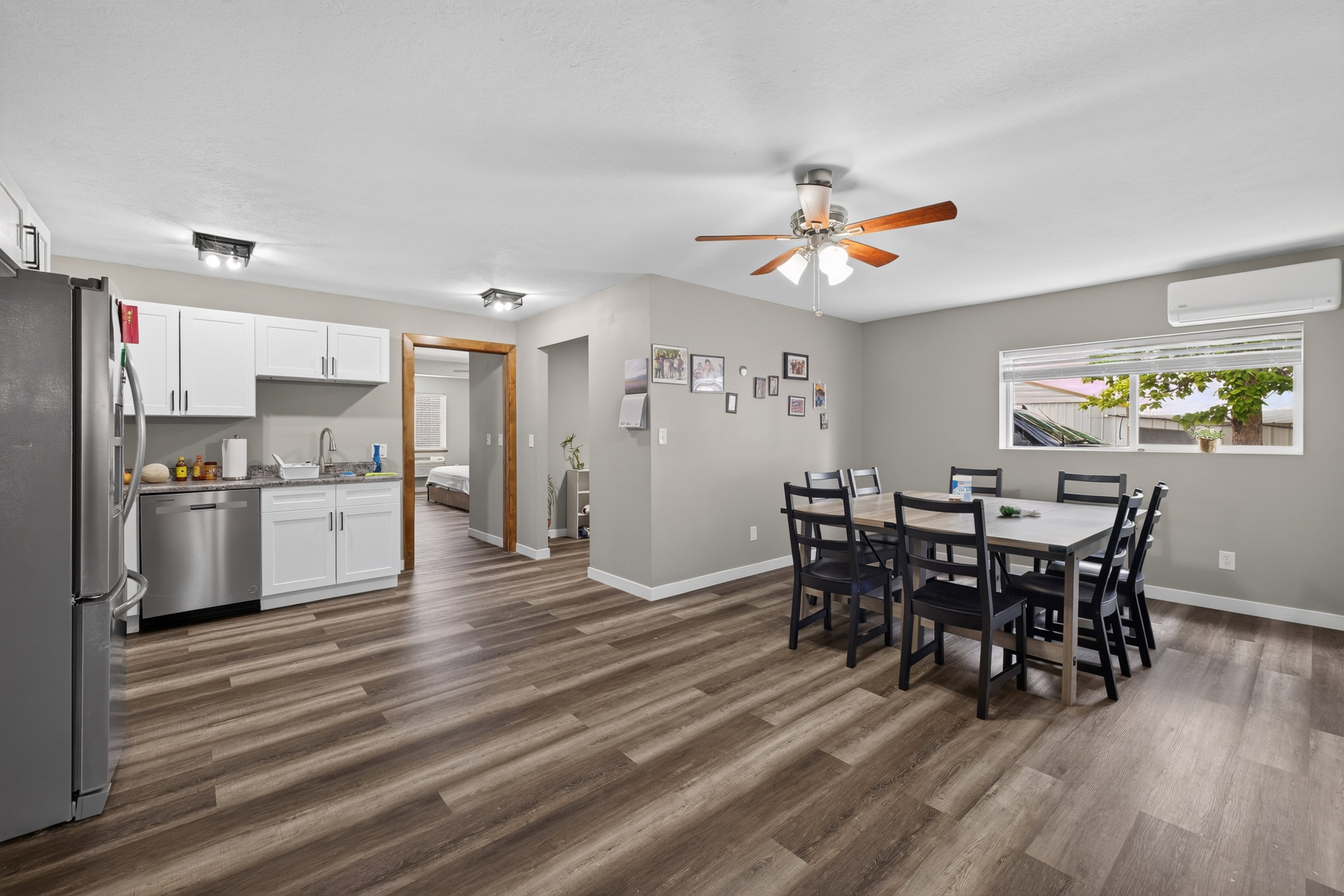 Open-concept living area featuring wood-finish flooring, a ceiling fan with integrated lighting, and a window with blinds