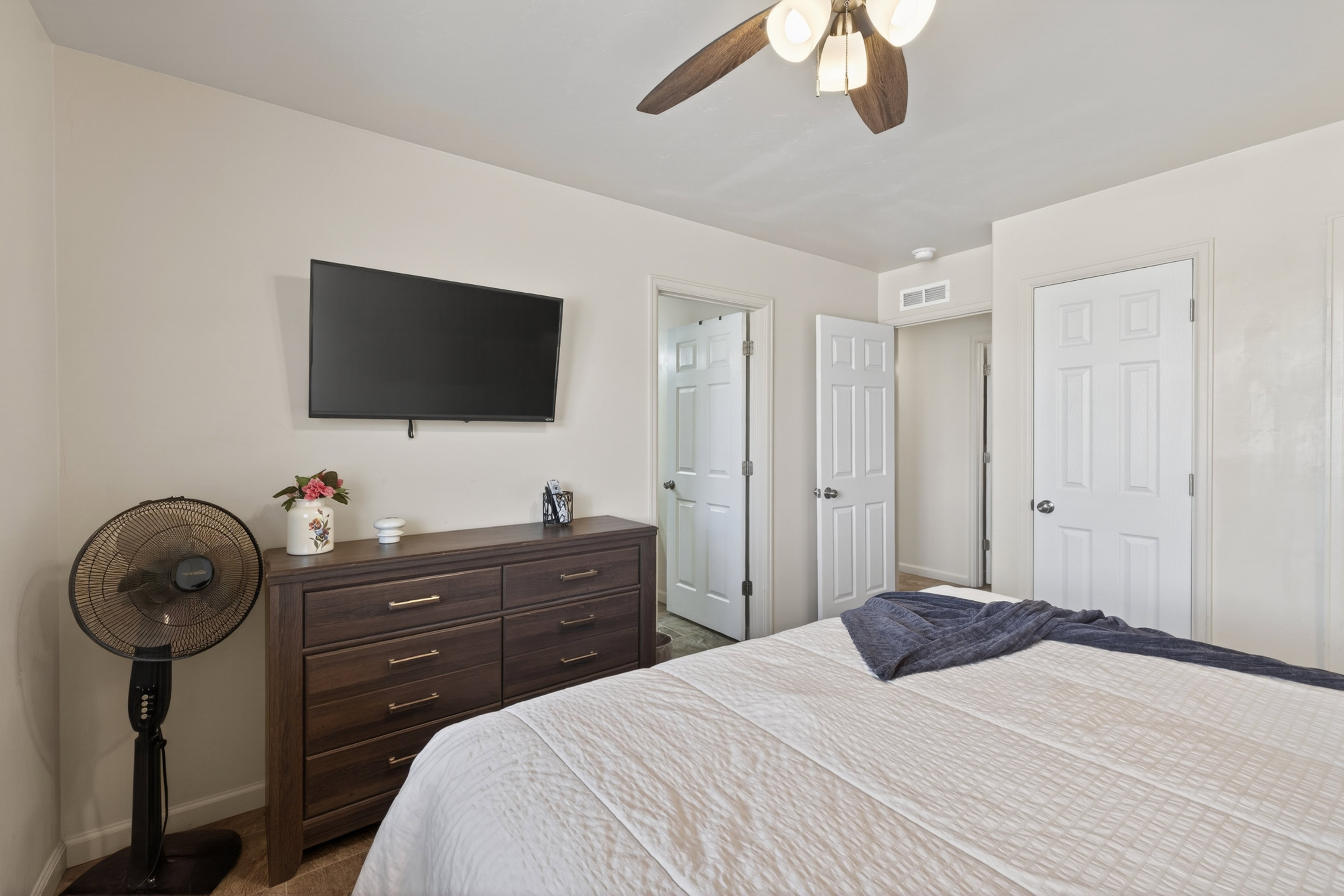 White paneled interior doors, a wood-finish ceiling fan with integrated lighting, and light-toned walls define this room