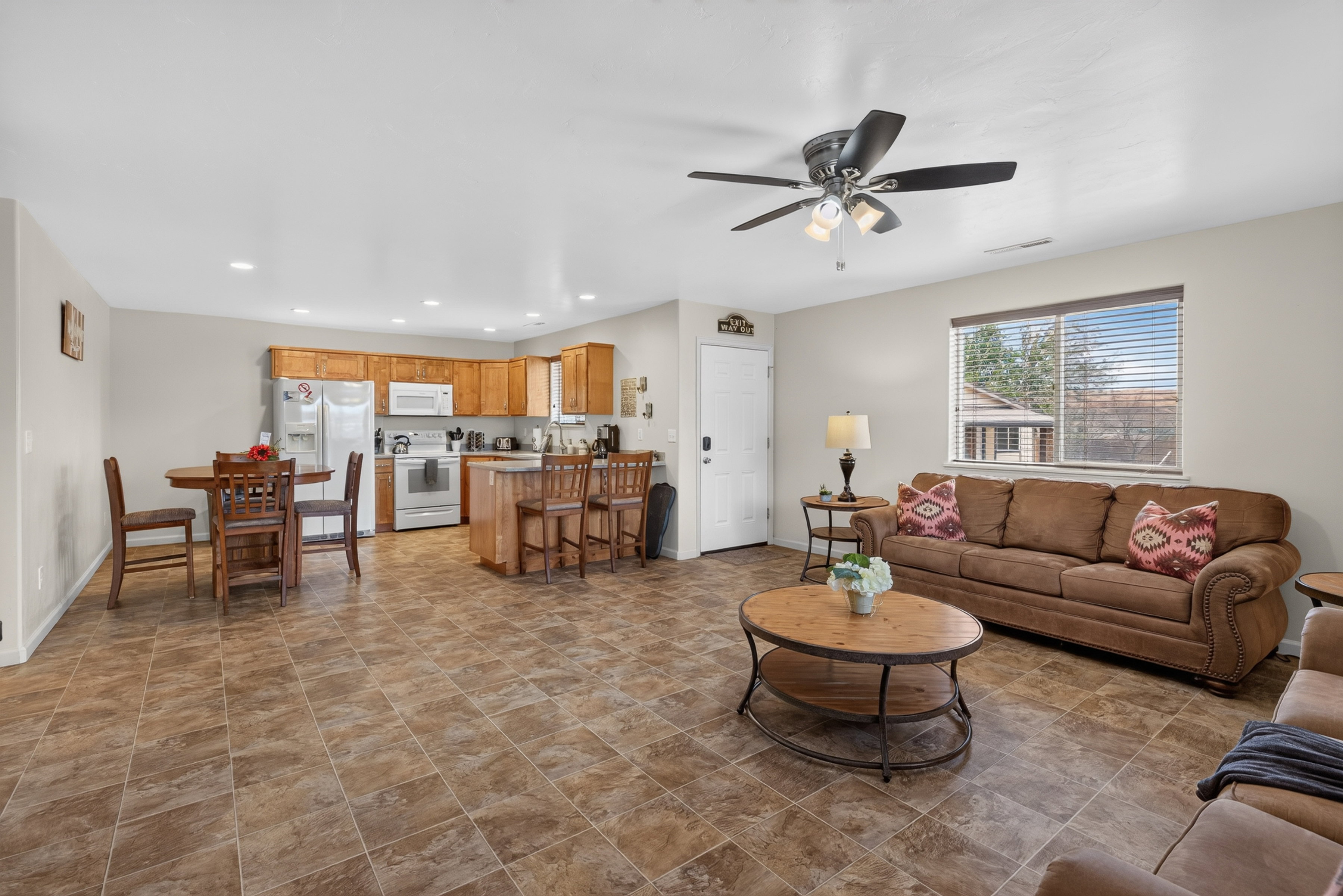 Open-concept living area featuring tile flooring, a kitchen with wood cabinetry and white appliances, a dining area, and a ceiling fan