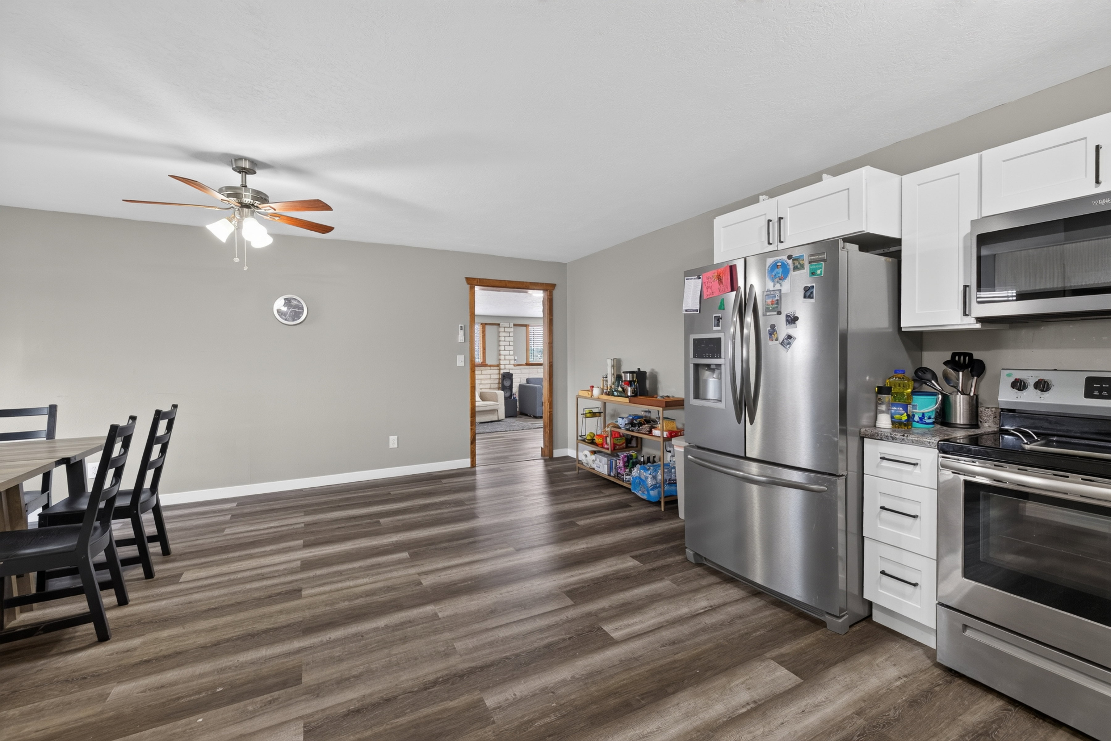 Kitchen and dining area featuring wood-finish flooring, white cabinetry, stainless steel appliances, and a ceiling fan with integrated lighting