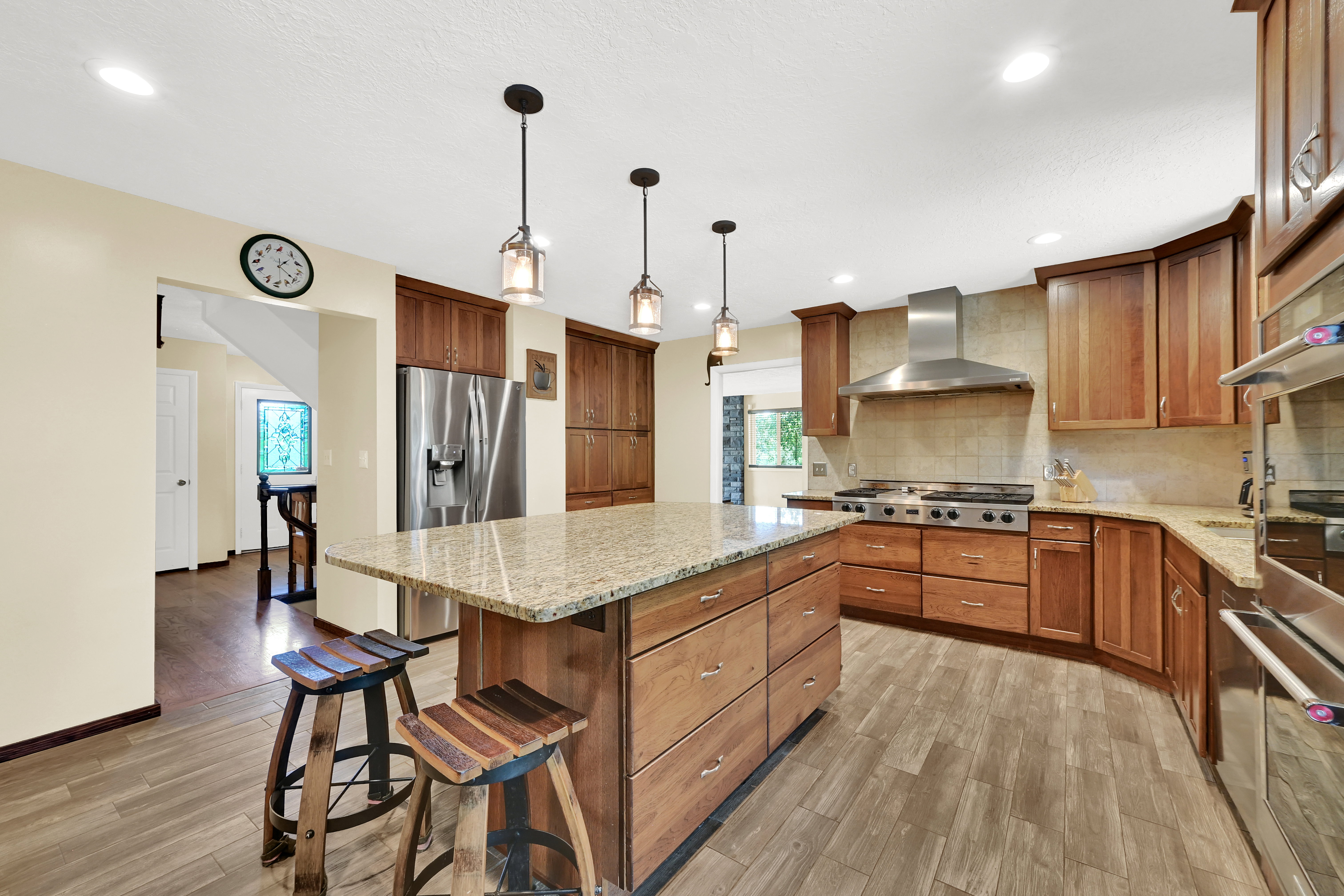 Spacious kitchen featuring a central island with a light-toned countertop, wood-finish cabinetry, stainless steel appliances, and wood-look flooring