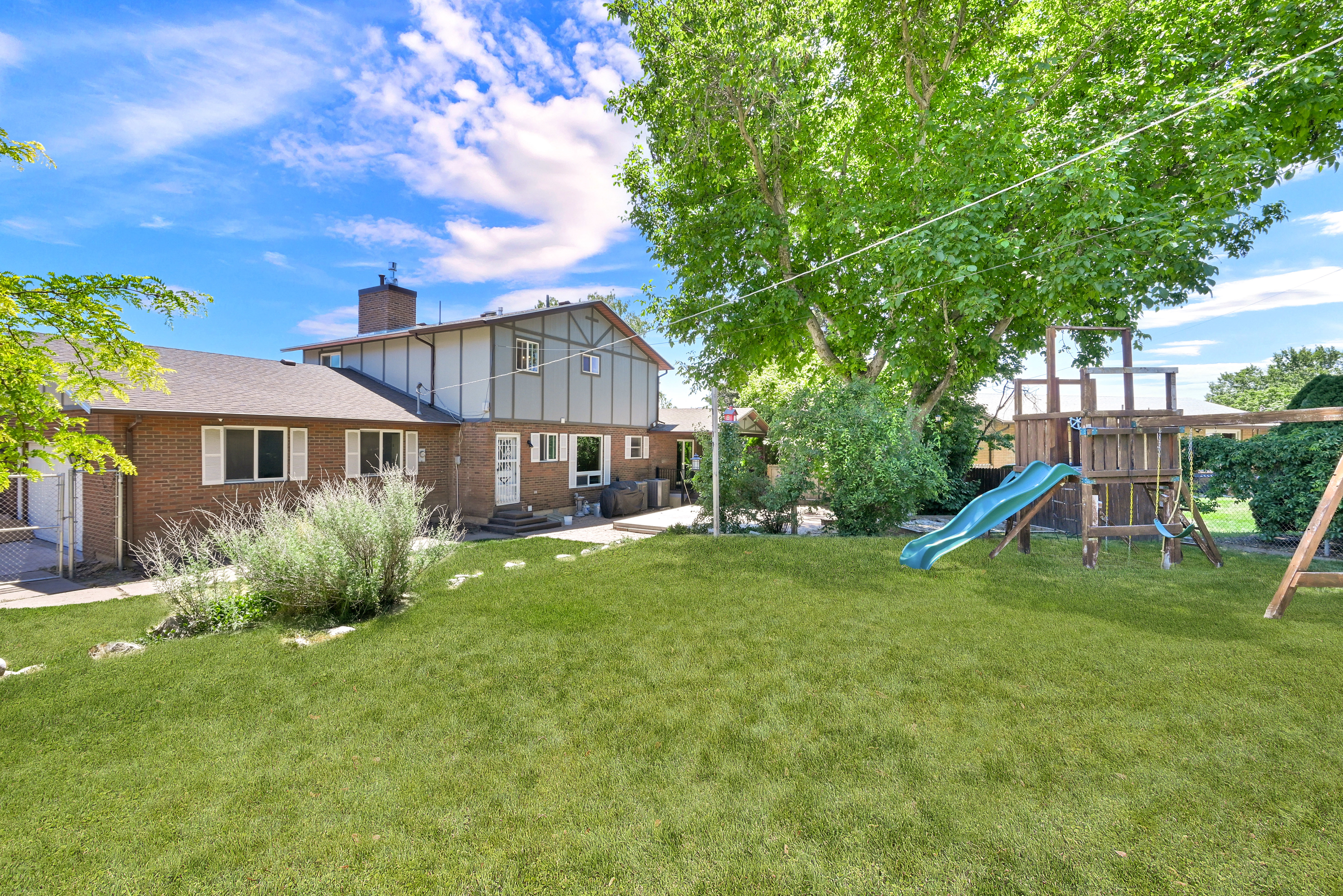 Expansive green lawn with mature shade trees, a brick and siding exterior, and a multi-level deck and patio area